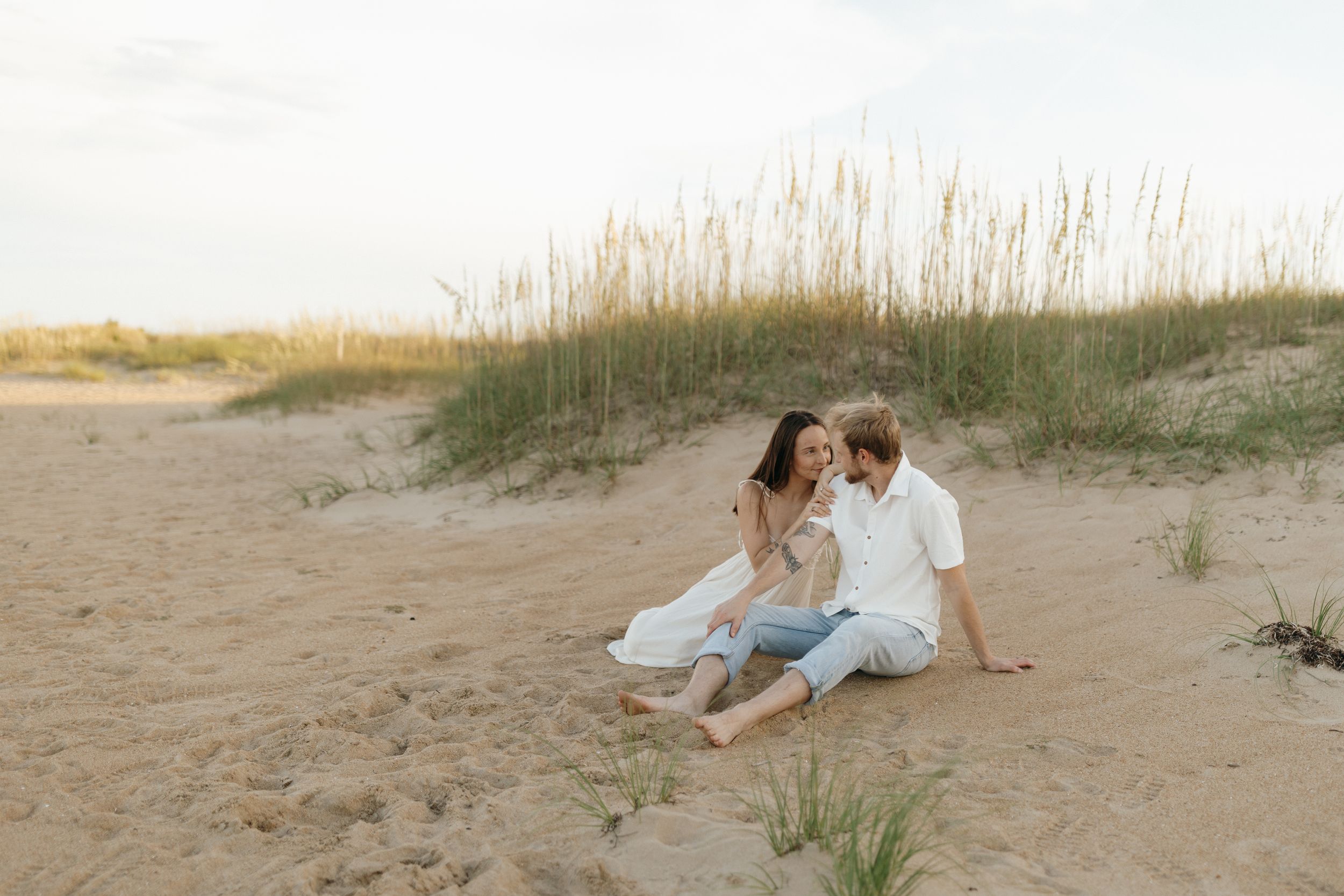 Couple sitting intimately together on a sandy beach during a romantic photoshoot.