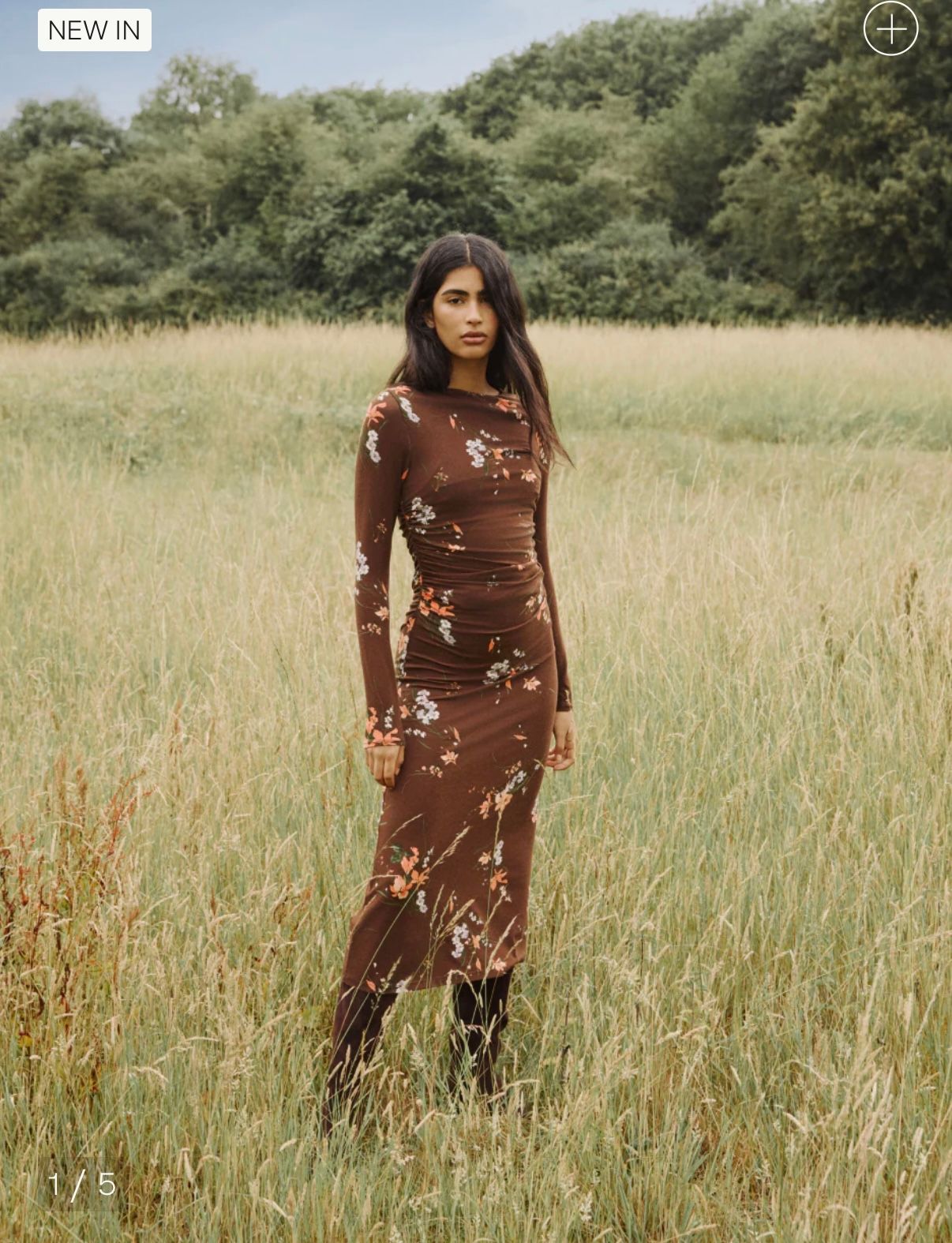 Person wearing brown floral dress poses in tall grass field on sunny day.