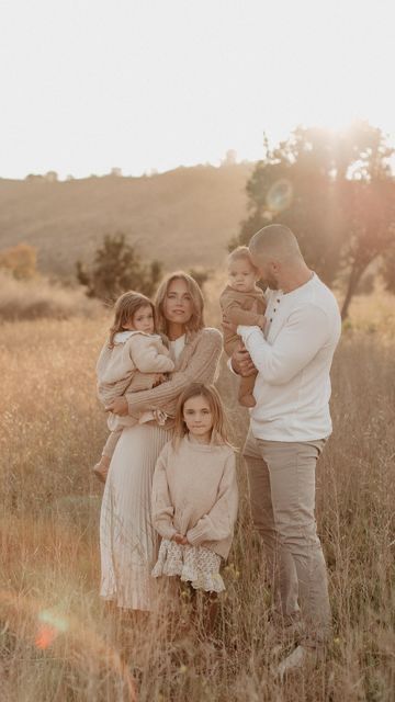 A family poses together in a sunlit meadow during golden hour wearing neutral colored clothing.