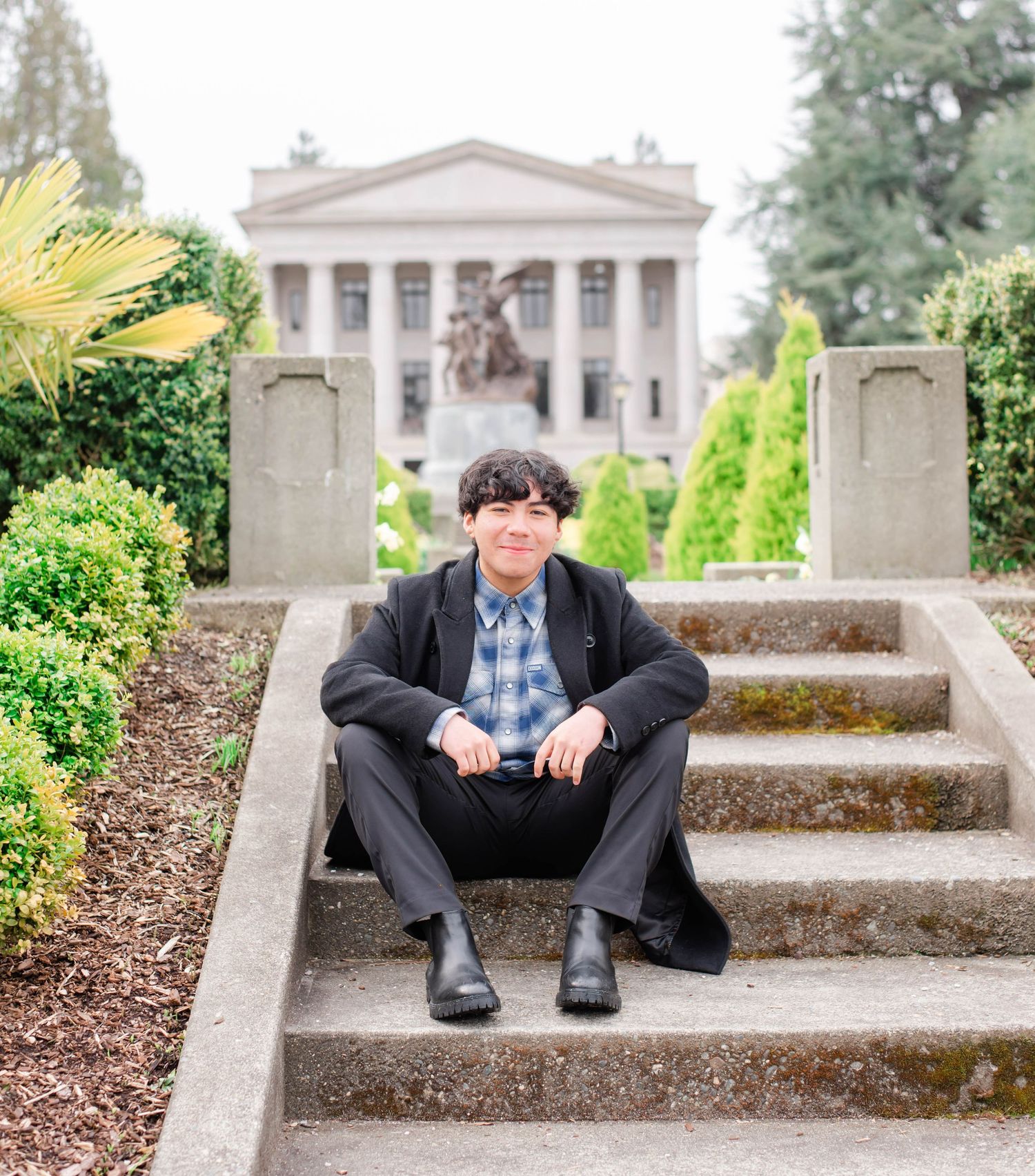 Person in dark jacket sits on concrete steps with classical building in background.