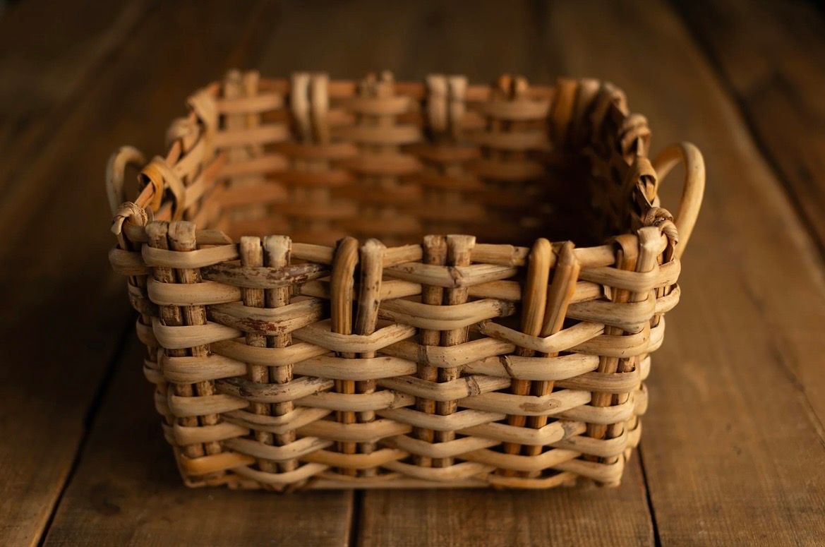 Empty woven wicker basket in heart shape sits on rustic wooden table surface.
