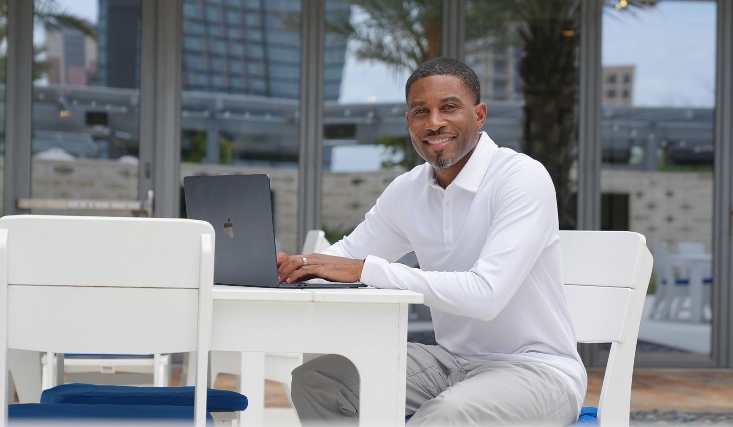 Three people in white shirts sit at a modern office desk while working on laptops and tablets.