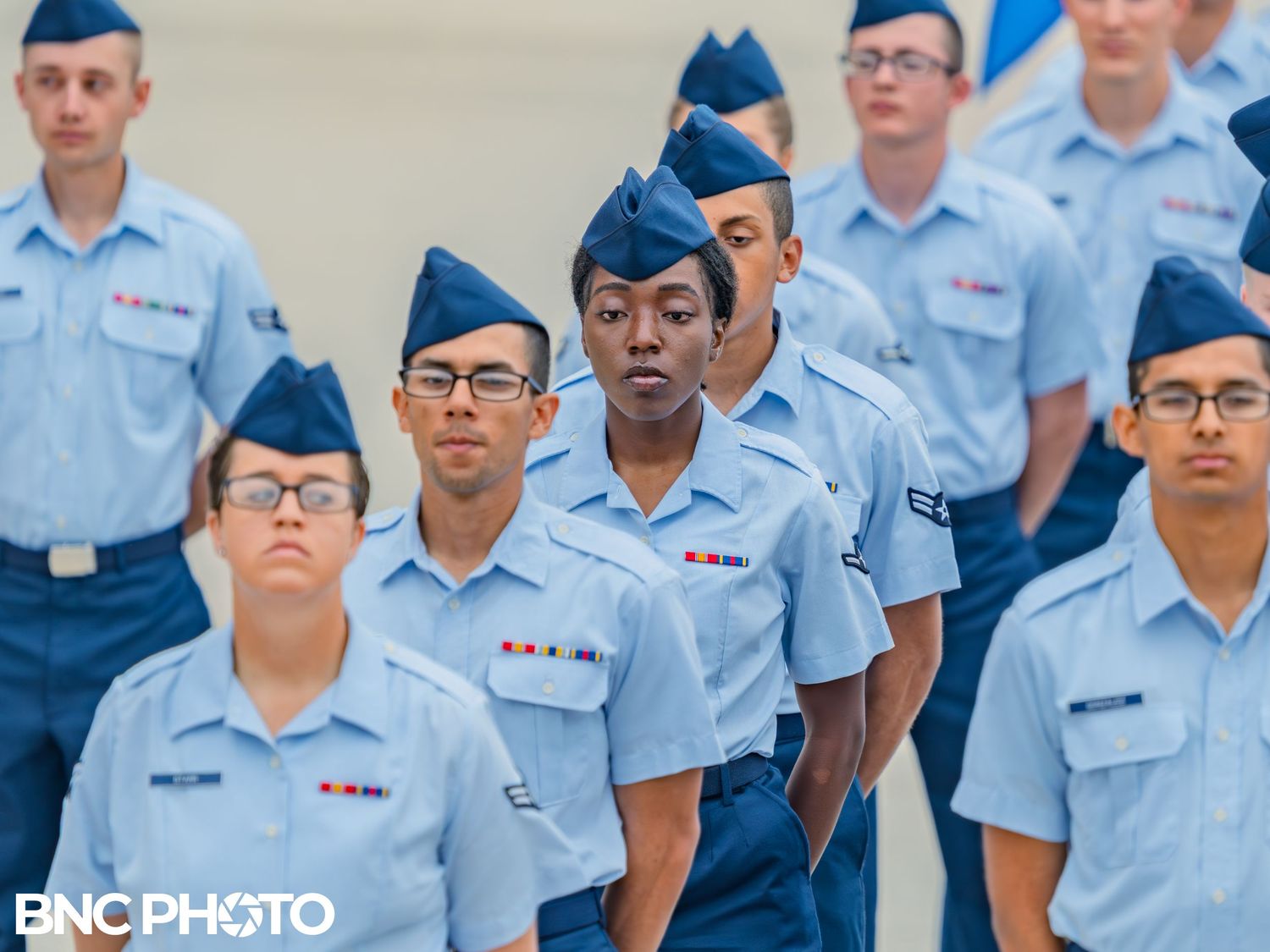 United States Air Force trainees lined up in formation wearing light blue shirts and dark blue trousers during a graduation ceremony.