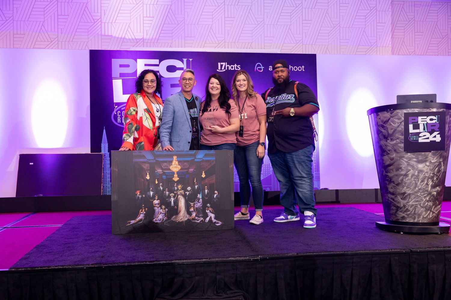 Four people posing on a purple-lit stage at a conference, holding a decorative artwork display.