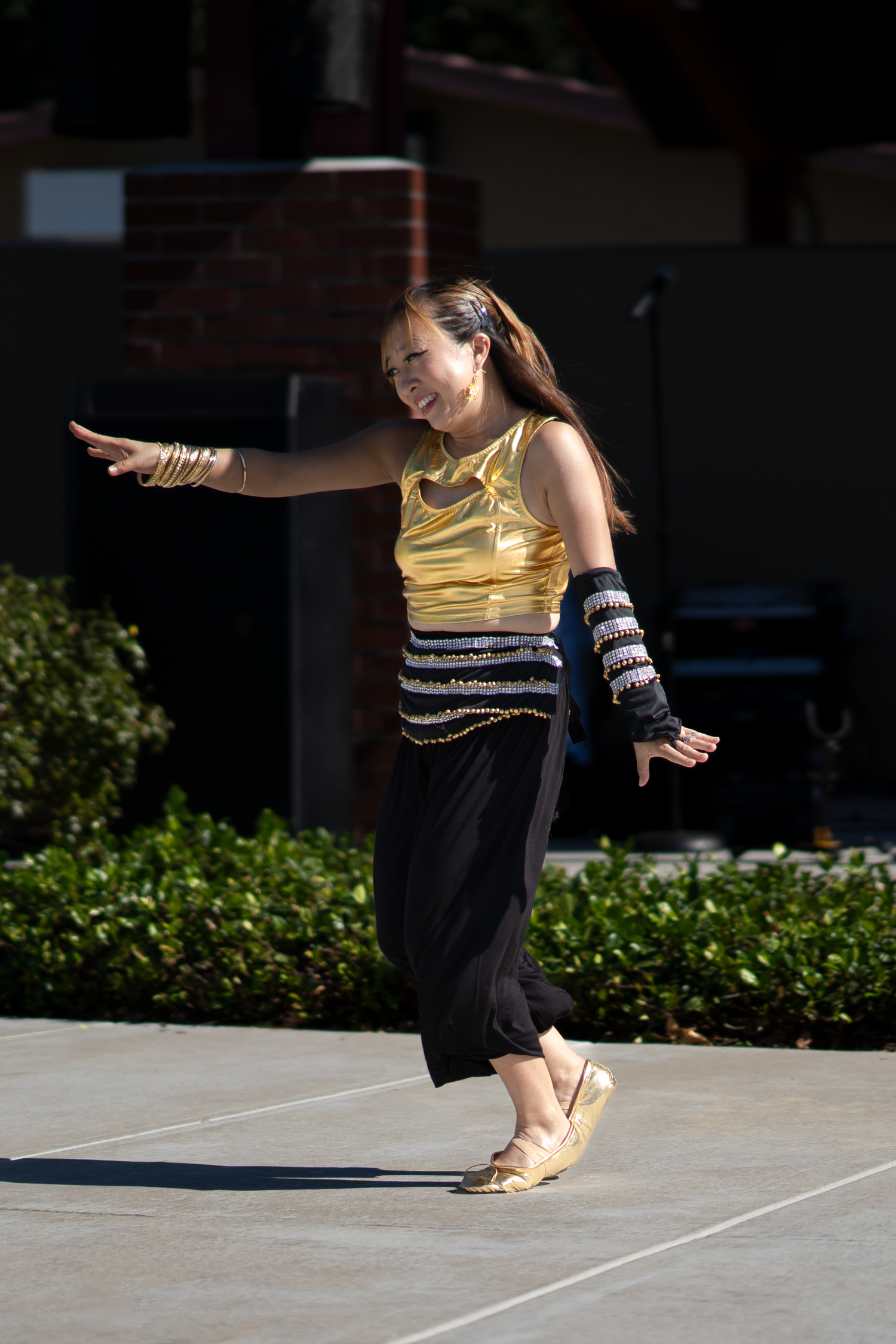 Dancer in yellow and black outfit performs graceful movements on outdoor stage.