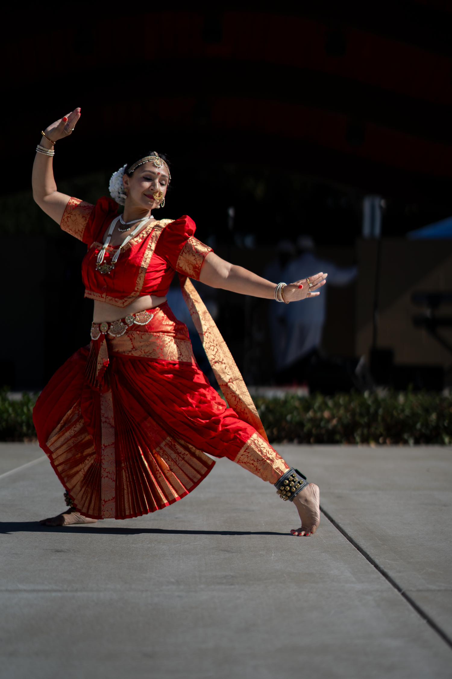 Traditional dancer in red costume performs dramatic floor movements in outdoor setting.
