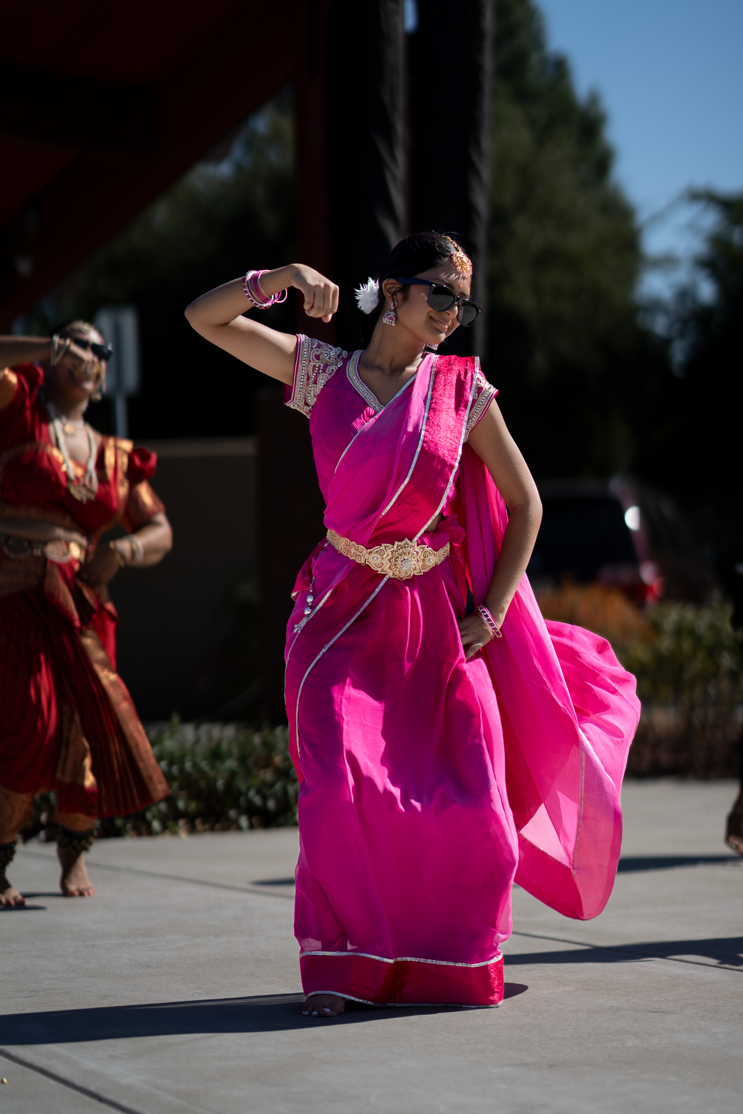 Performer in bright pink dress flows through graceful dance movements outdoors.