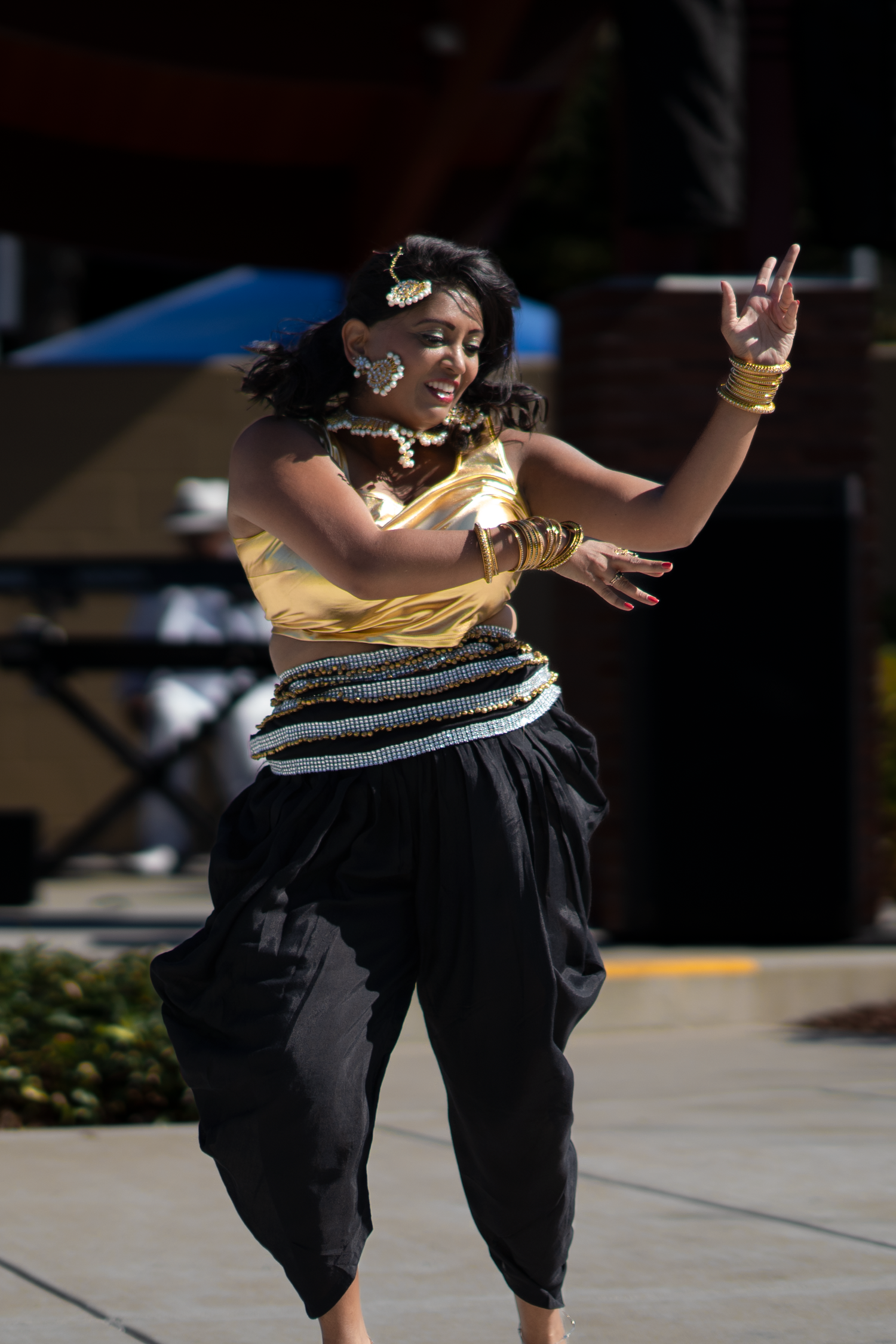 Dancer in yellow top and black pants performs expressive movements on outdoor stage.