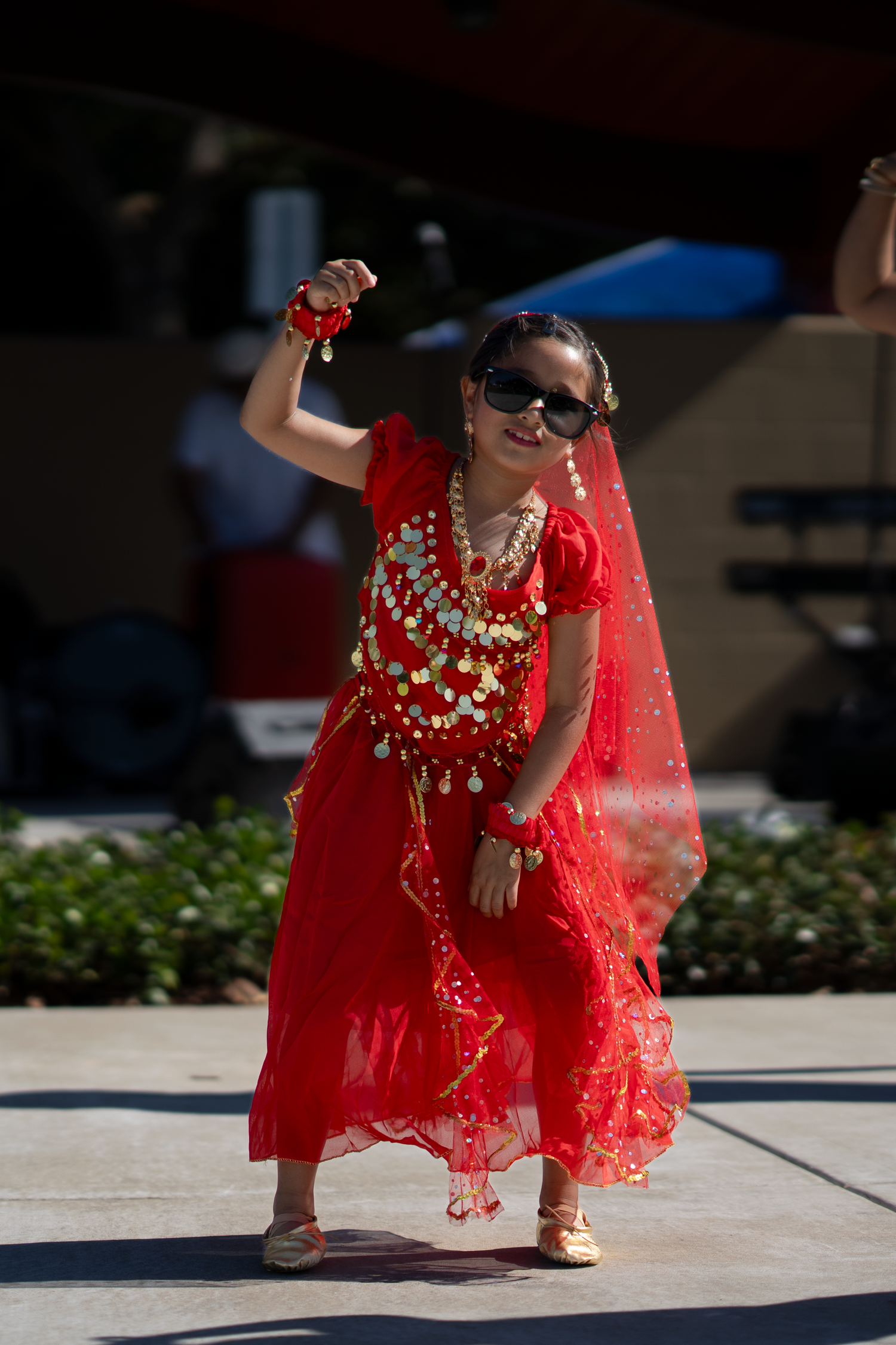 Dancer in sparkly red traditional dress with gold accents performs cultural dance.