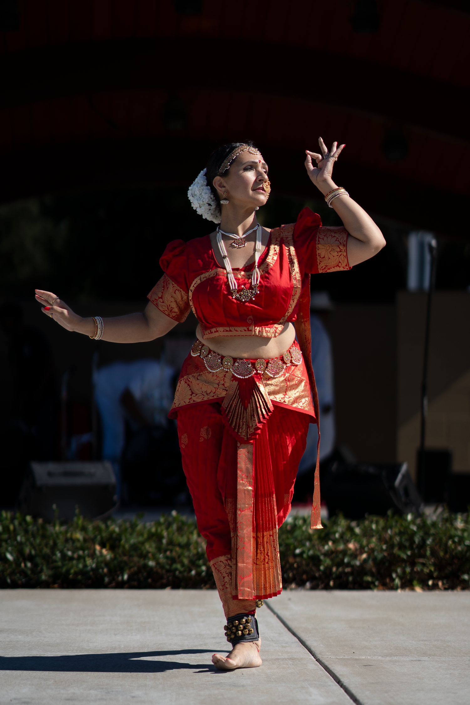 Dancer in red traditional costume demonstrates expressive dance movements outdoors.