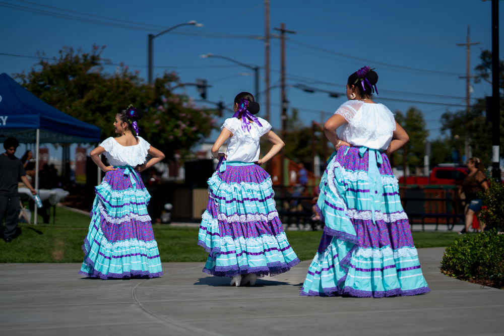 Line of dancers in turquoise and purple traditional Mexican dresses perform in formation.