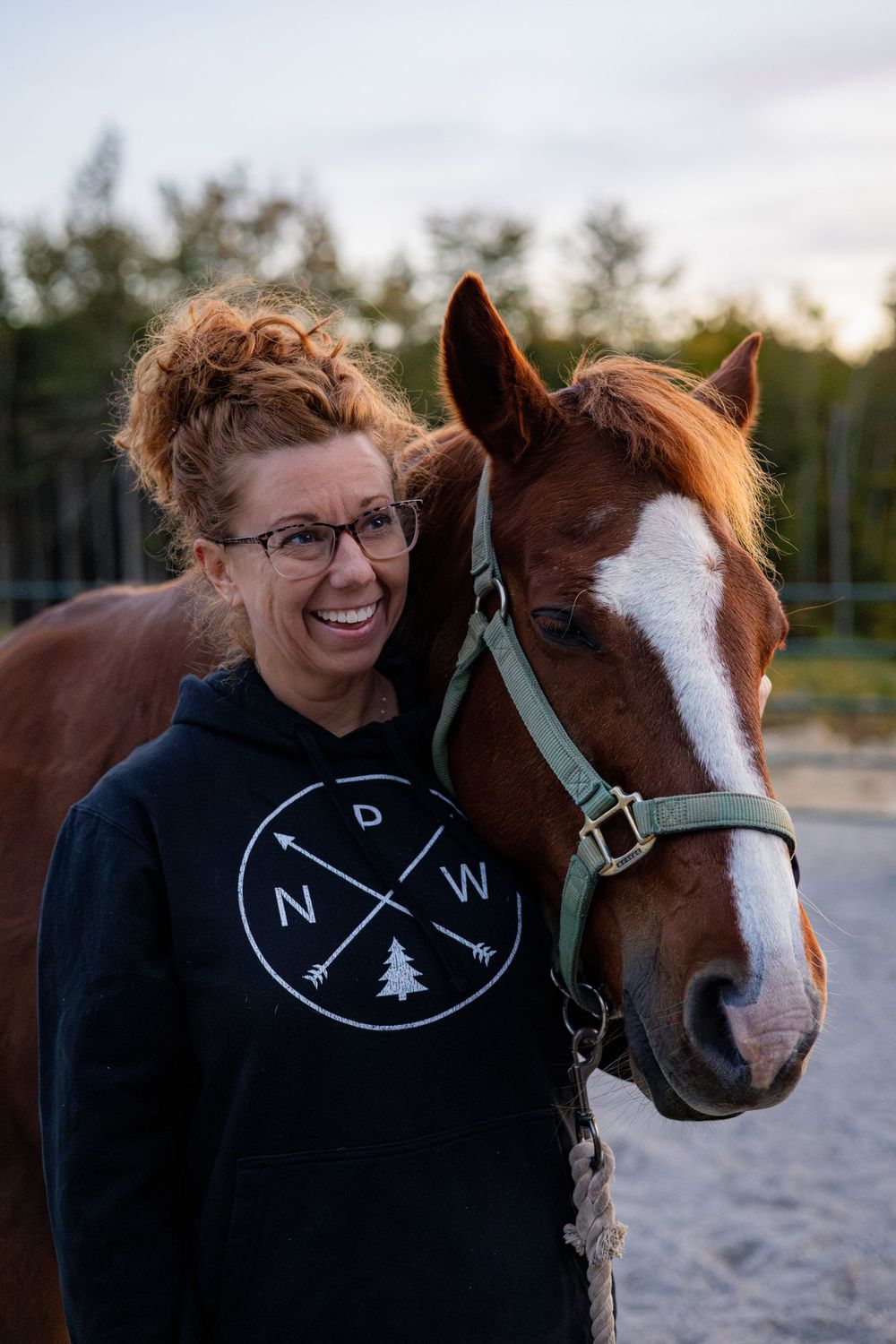 A person wearing a navy sweater shares tender moments with a brown and white horse outdoors.