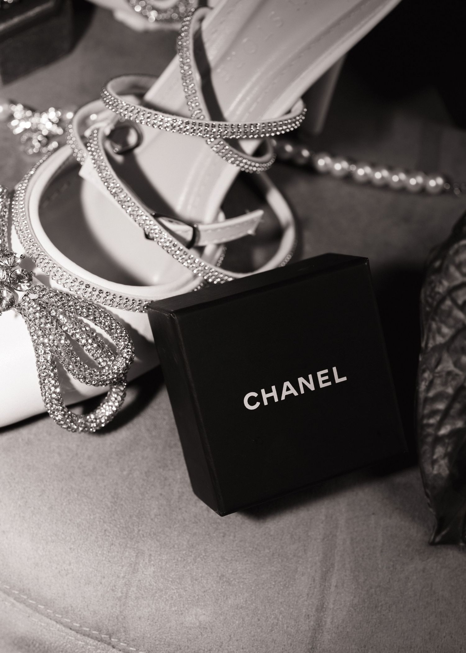 Black and white close-up of Chanel jewelry box beside crystal bow bridal heels and pearl accessories.
