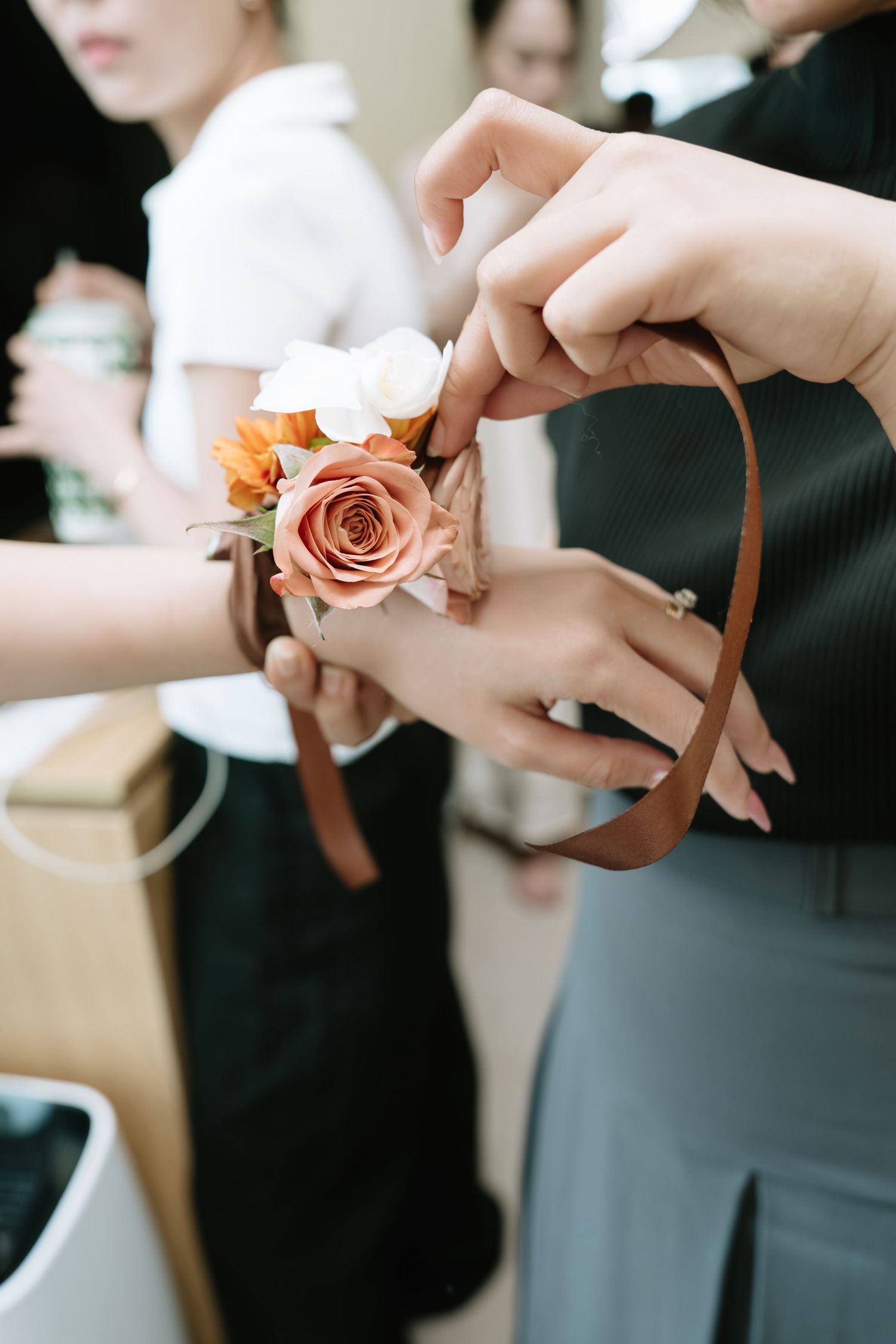 Bridesmaid receiving a floral wrist corsage with peach rose tied with brown ribbon.