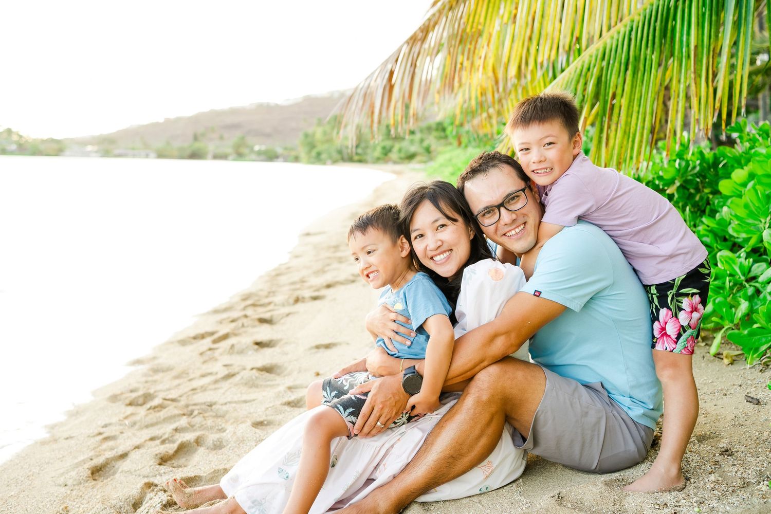 A family relaxes together on a tropical beach during sunset with palm trees in the background. Oahu family photography, Hawaii family photo