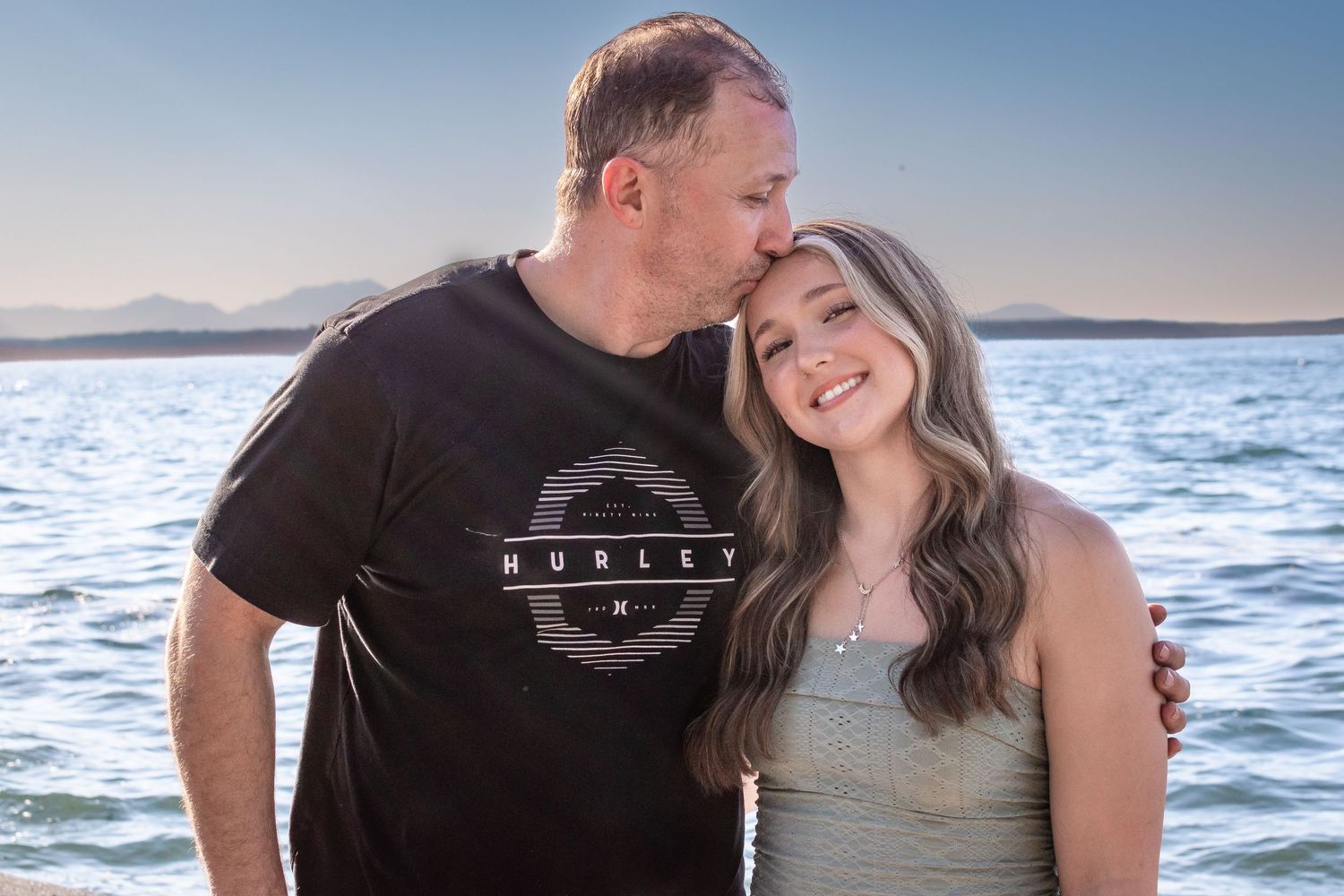 Dad kissing his daughter’s forehead at Alki Beach in Seattle during emotional senior portraits.