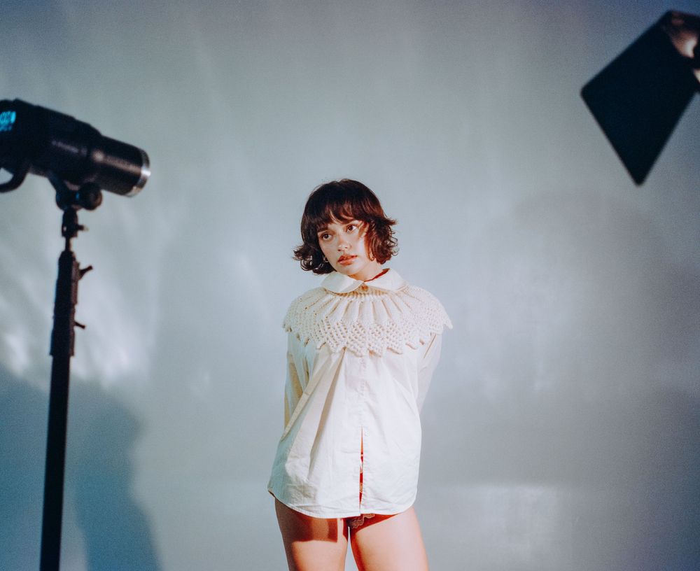 Studio fashion photo with lighting equipment and cream ruffled collar top.