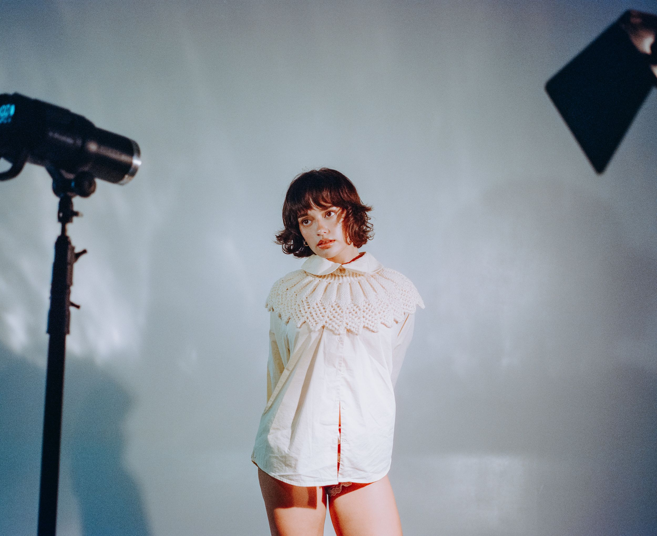 Studio fashion photo with lighting equipment and cream ruffled collar top.