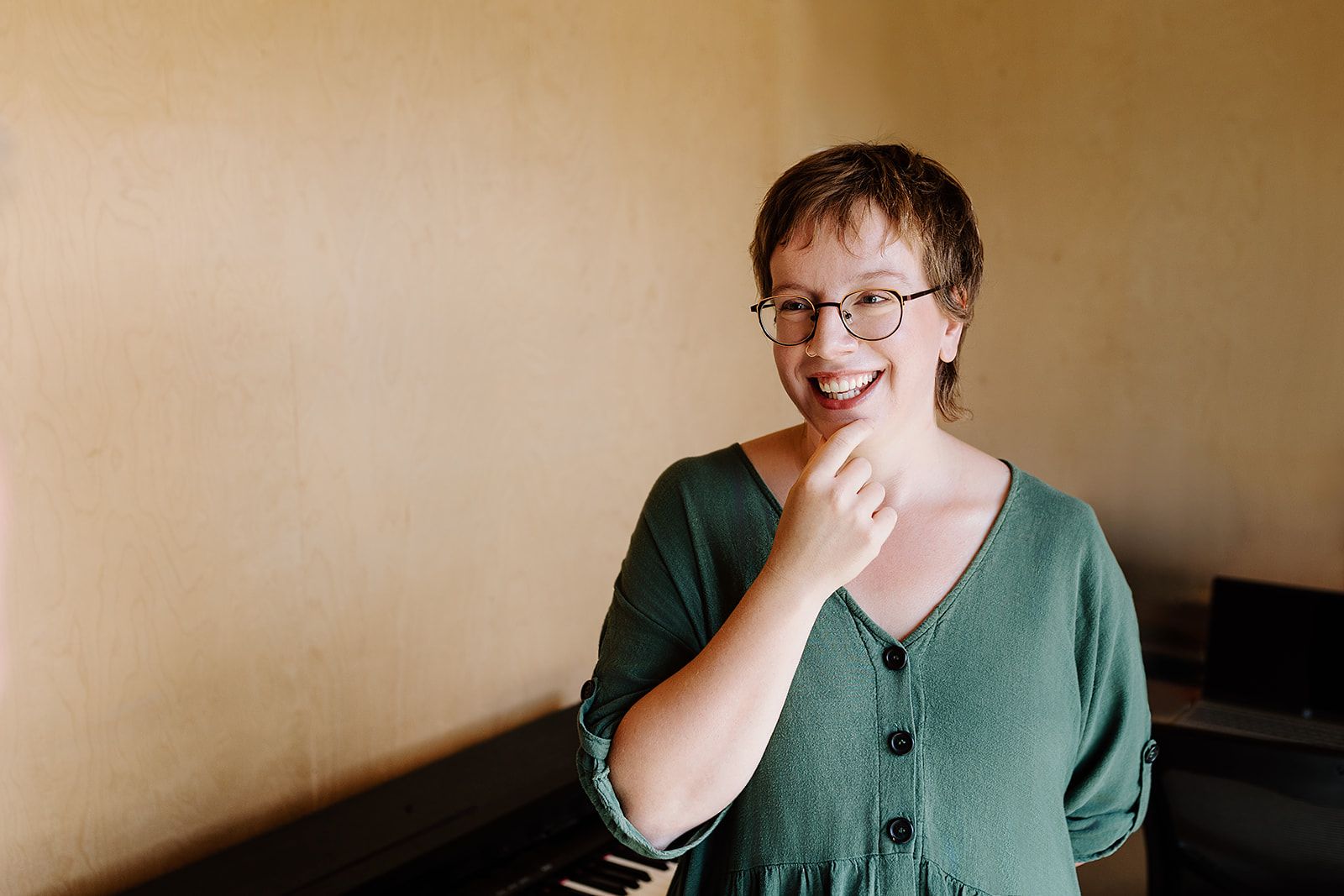 A joyful expression lights up someone's face while wearing glasses and a green cardigan against a neutral wall.