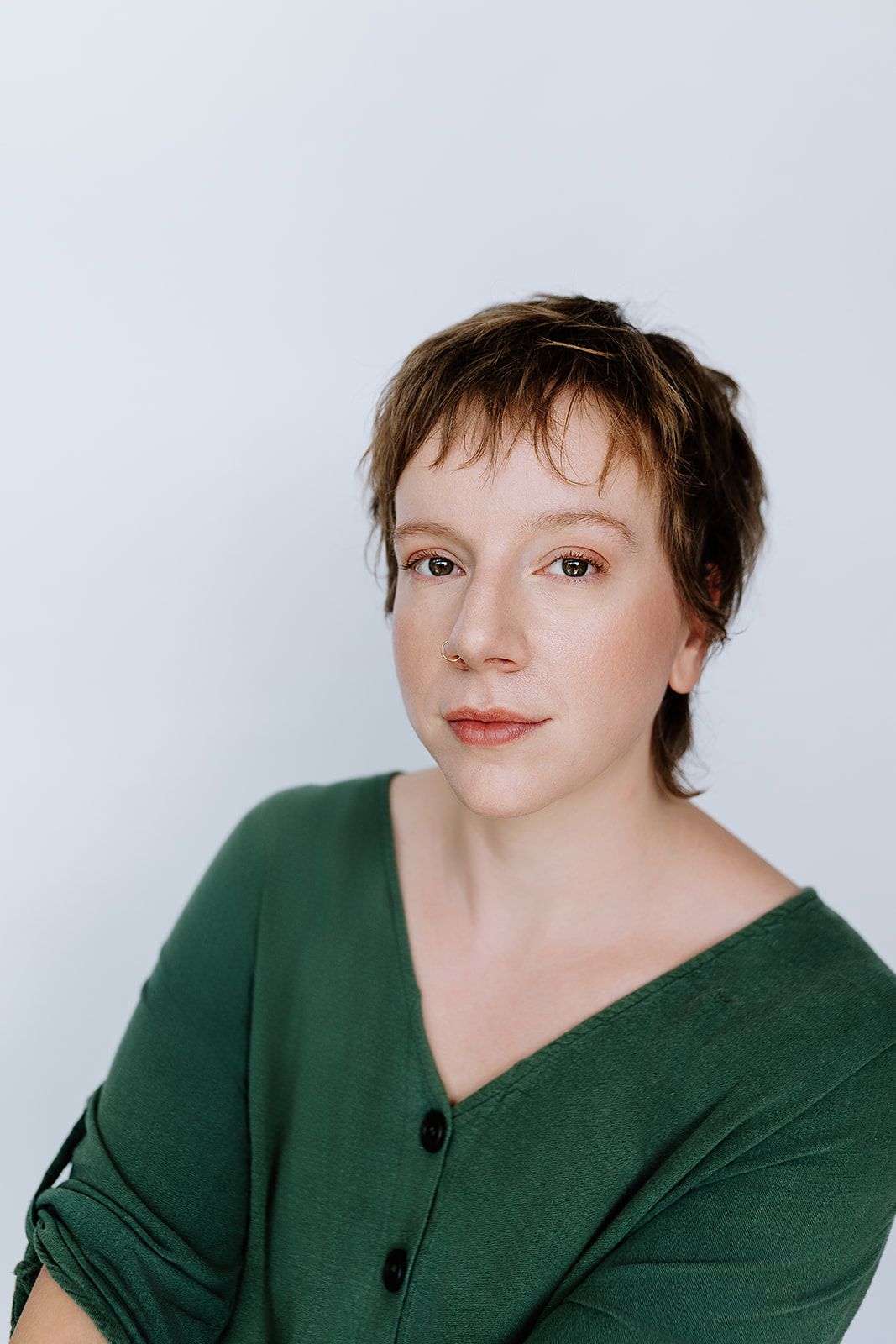Studio portrait with dark green sweater against light background showing contemplative expression and short brown hair.
