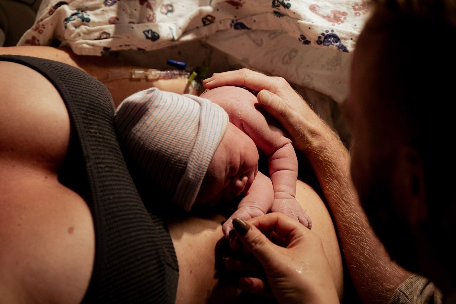 Close-up shot of hands gently holding a newborn baby wrapped in light colored clothing.