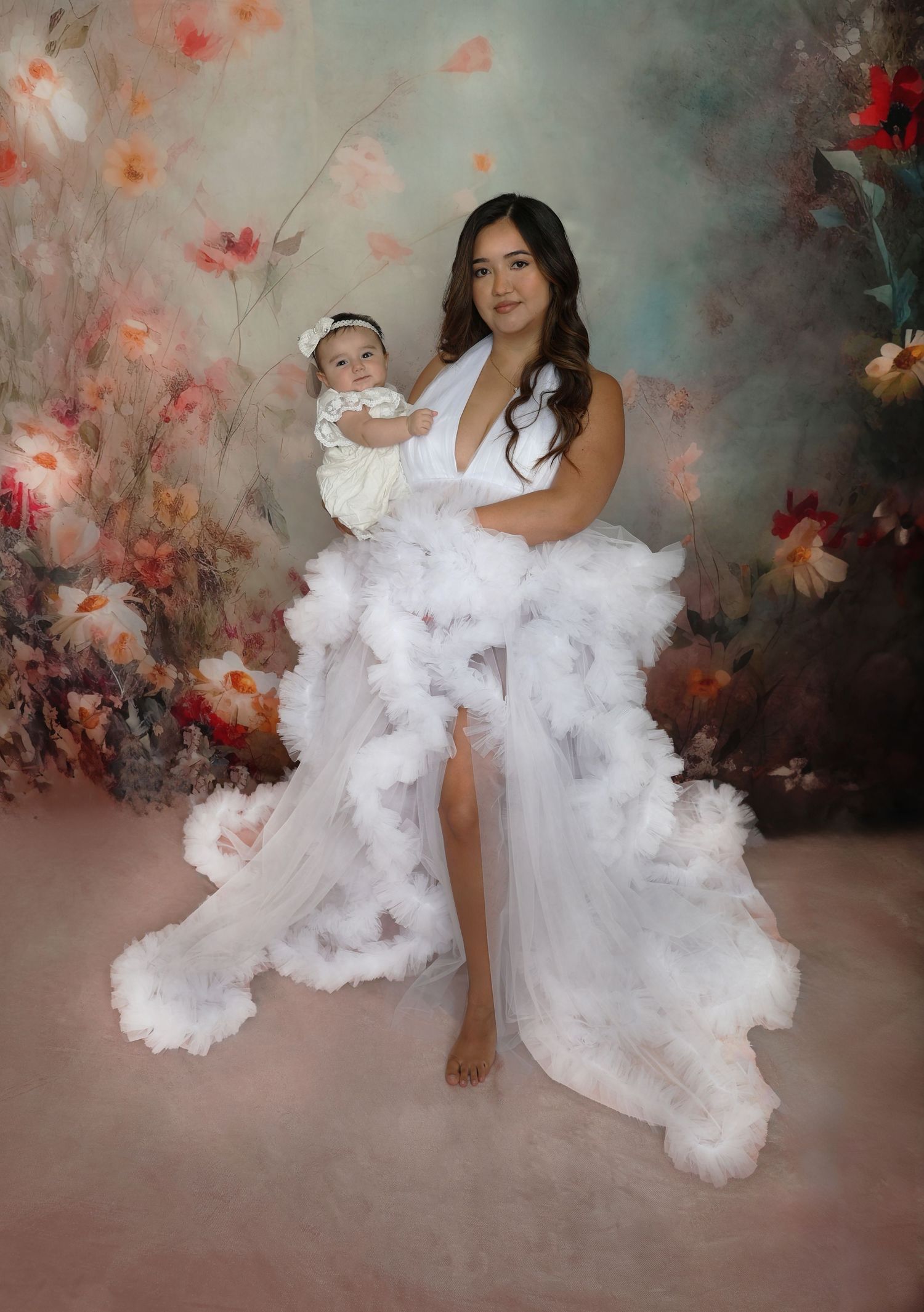 Artistic maternity portrait with dramatic white flowing dress against floral background.