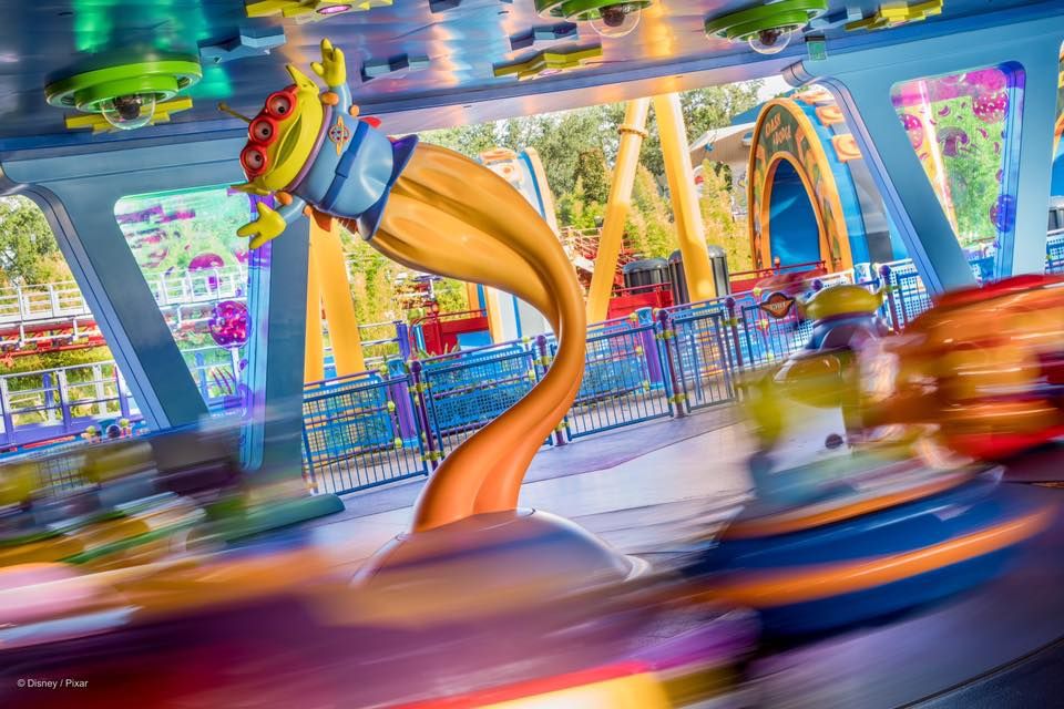 Motion-blurred colorful carnival ride with orange and blue swirling elements creates a vibrant abstract scene at an amusement park.