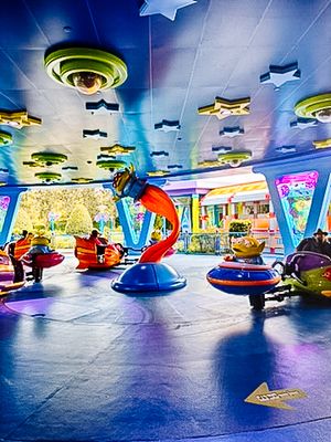 Colorful spinning teacup amusement park ride with vibrant lights and empty seats against a blue-lit indoor space.