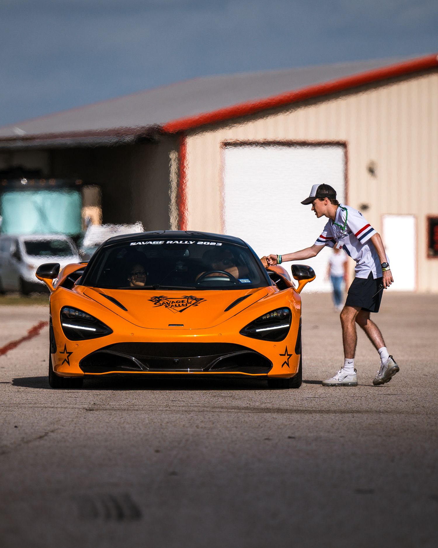 Bright orange McLaren supercar parked in front of industrial buildings.