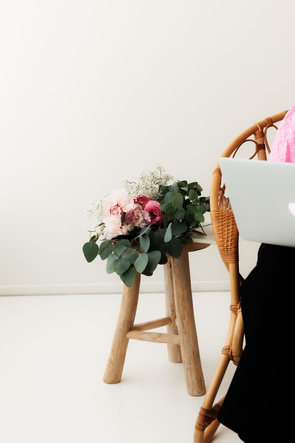 Pink and white floral arrangement with eucalyptus sits on wooden stool against white background.