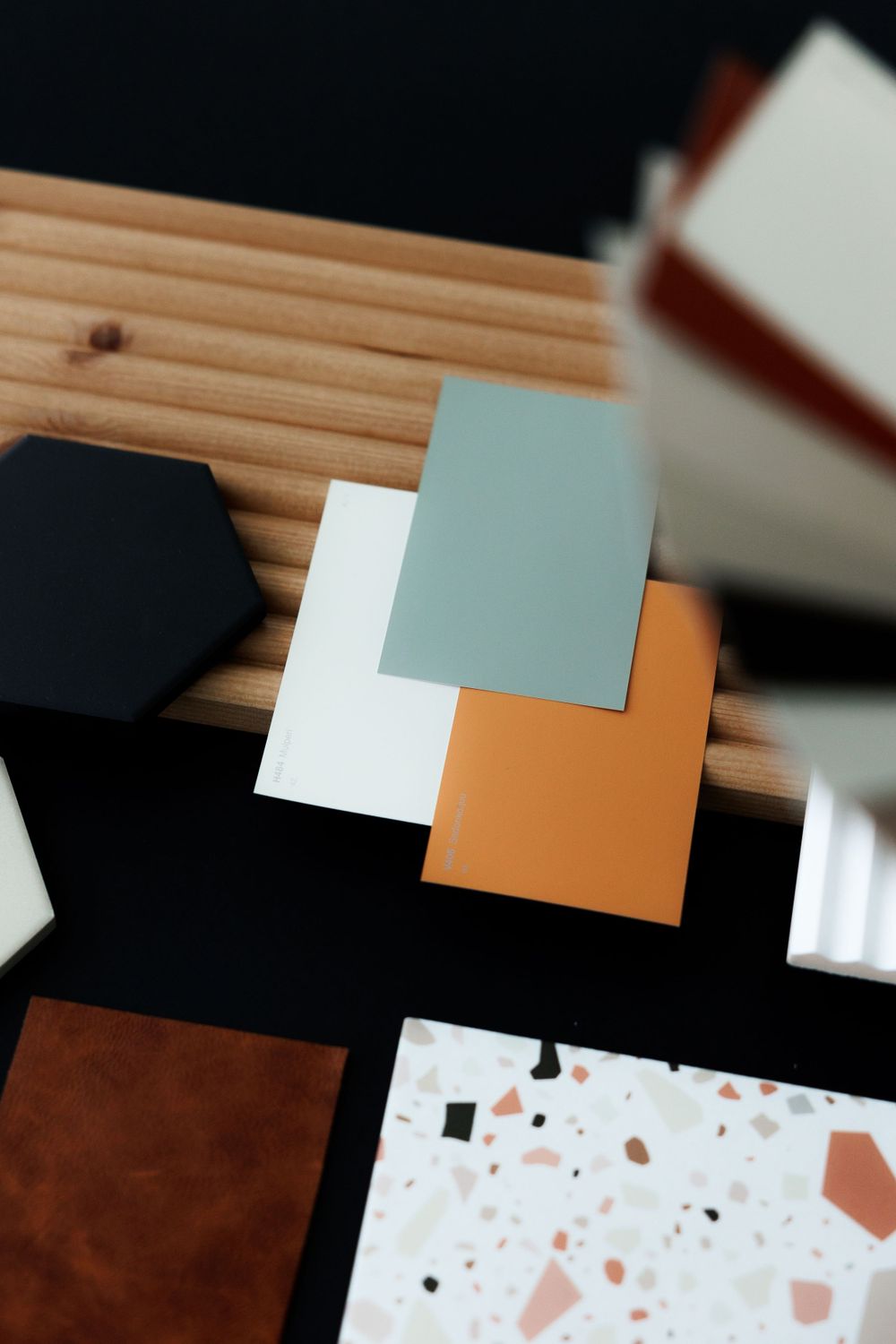 Collection of material samples including colored squares and terrazzo pattern swatches arranged on a wooden surface.