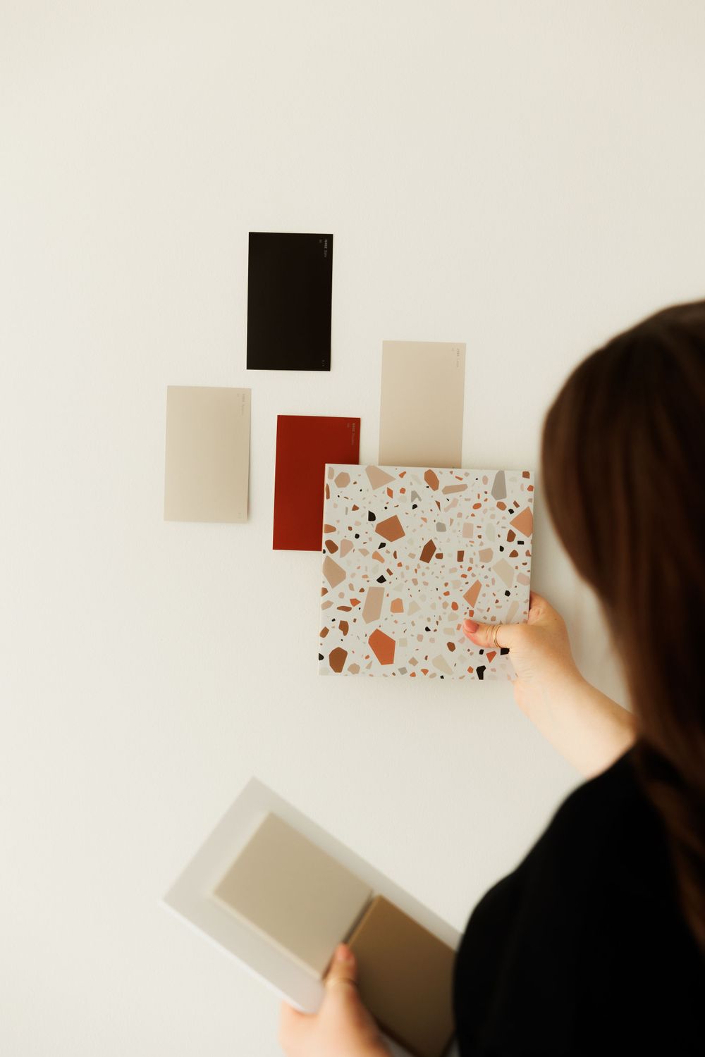 Person looking at color and material swatches displayed on white wall during interior design planning session.