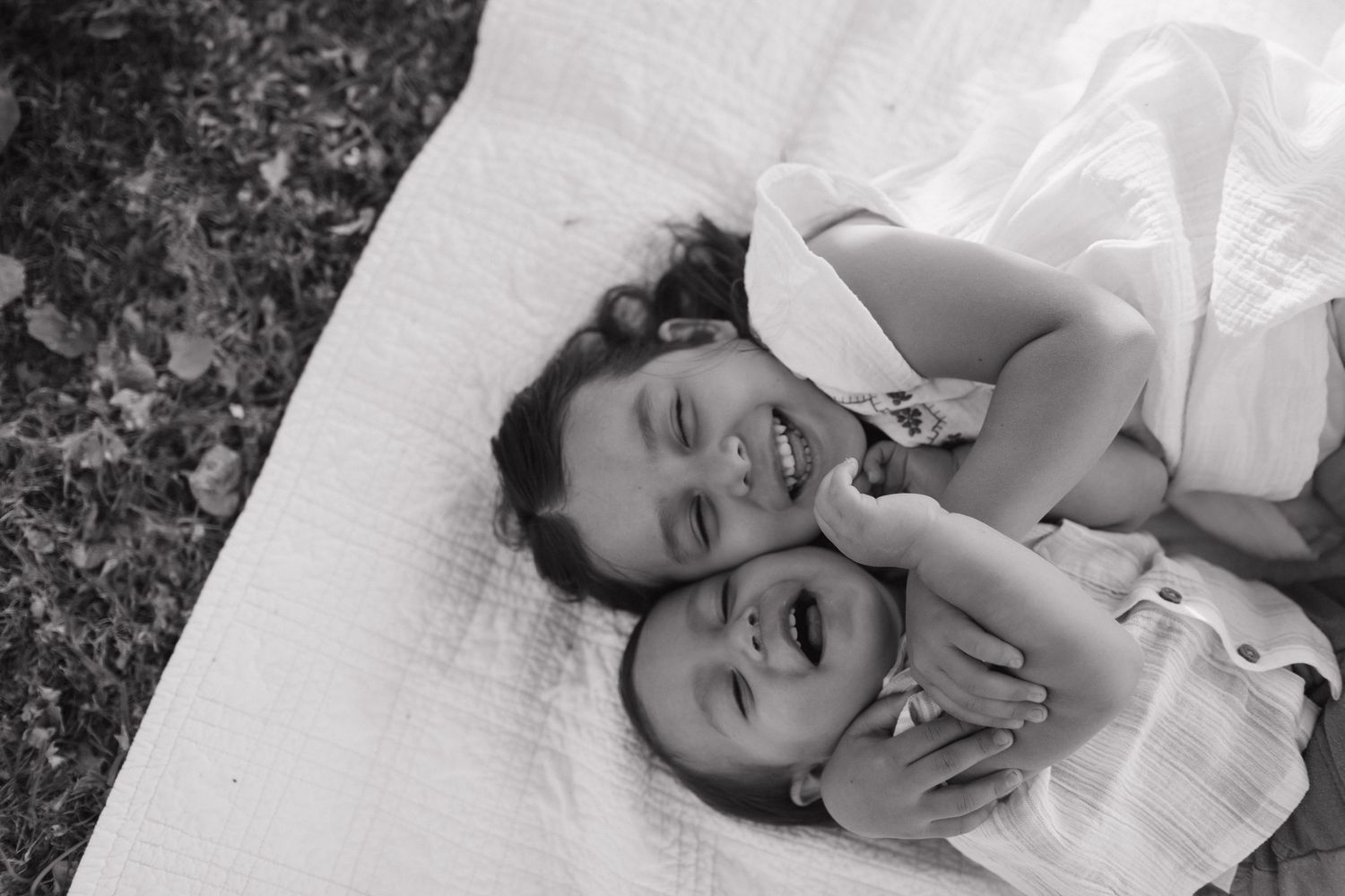 Family lounging together on white blanket under tree with flower bouquet during outdoor summer picnic.
