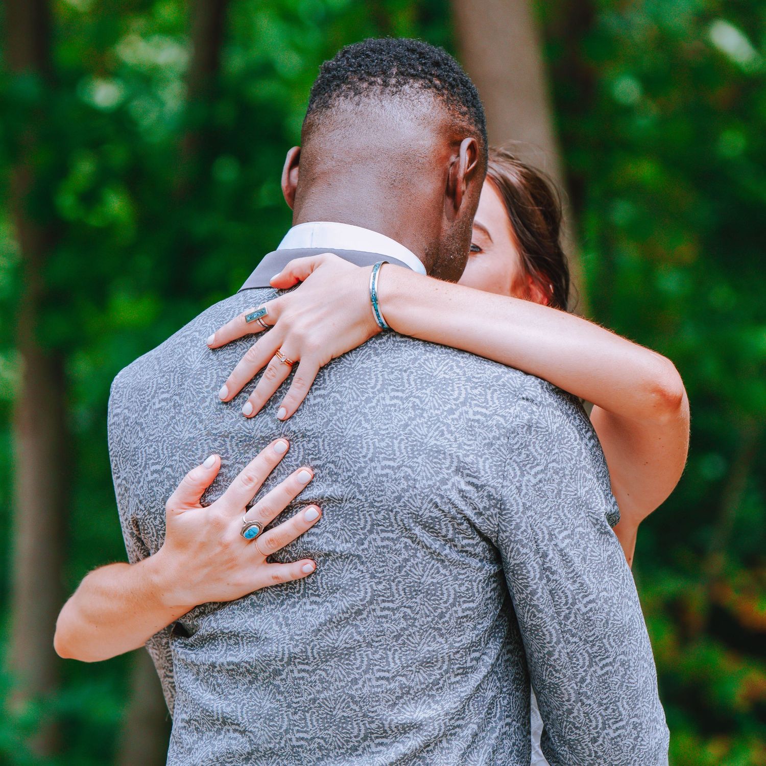 Close up of two people embracing in a tender moment outdoors with green foliage background.
