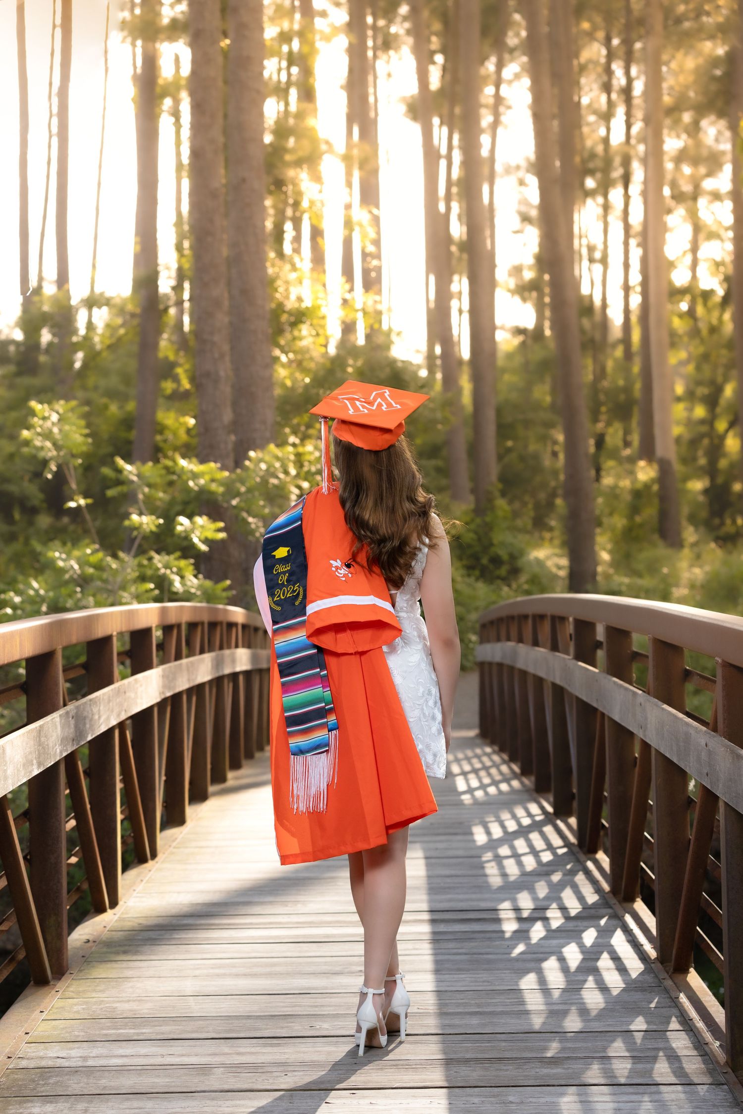 Graduation photoshoot in a garden setting at sunset with flowing black robe and white dress.