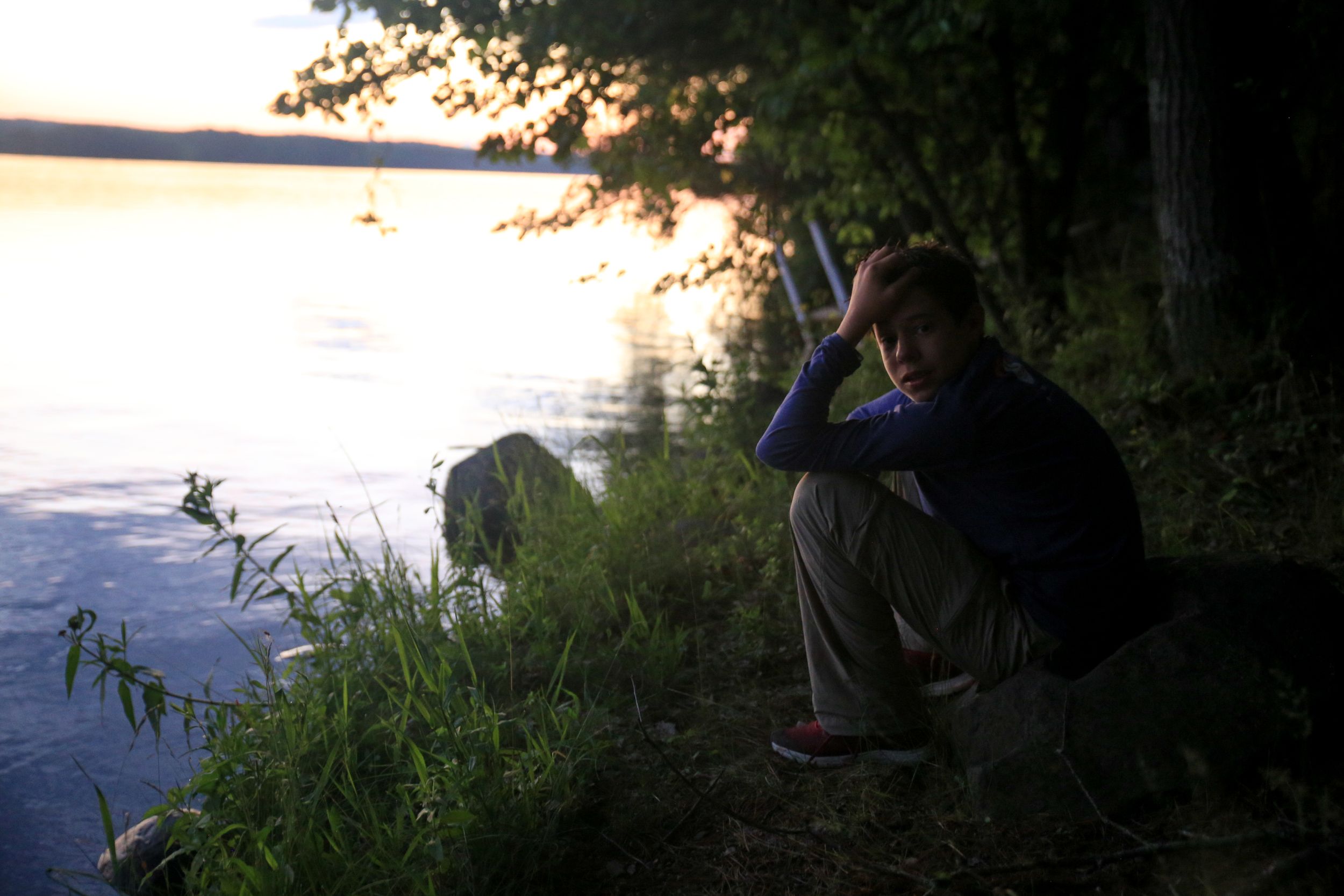 Silhouette of someone sitting by a lake at sunset watching the water.