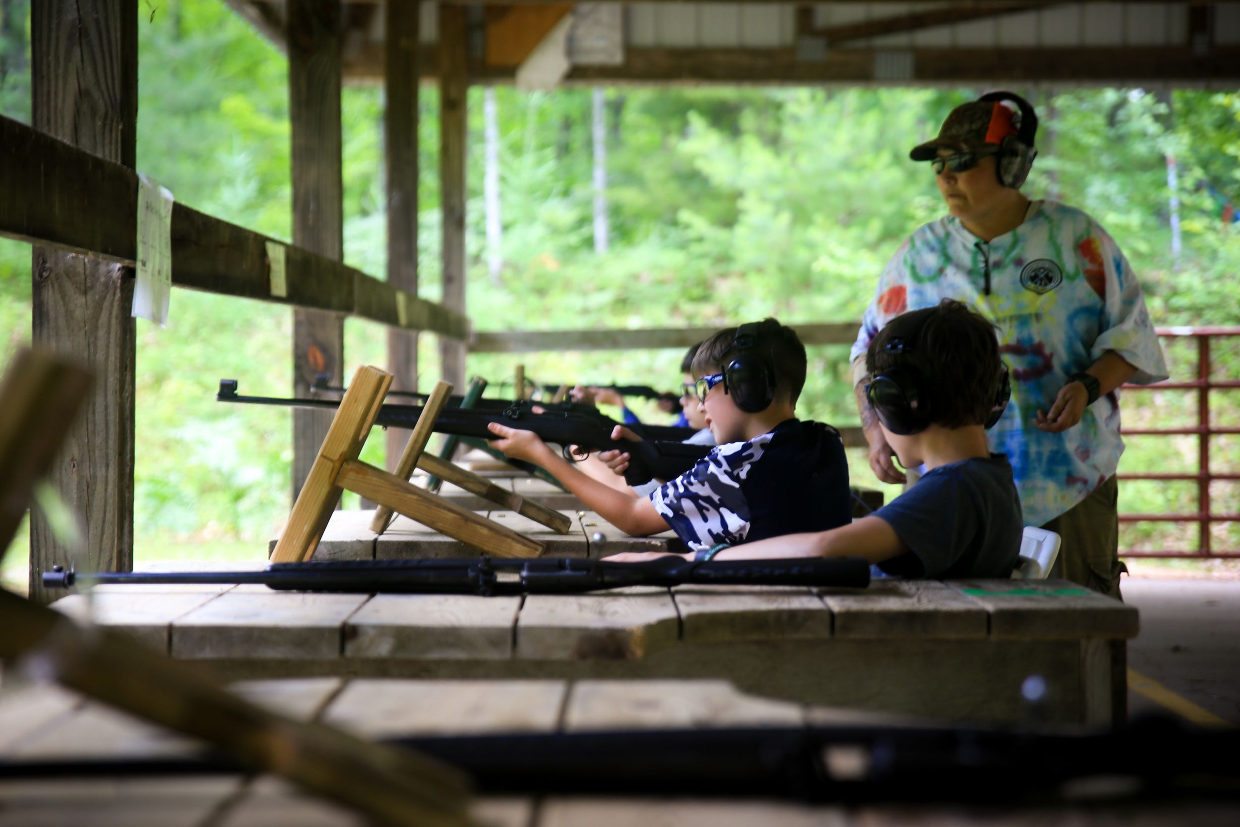 Campers practice rifle shooting at a covered outdoor range with supervision.