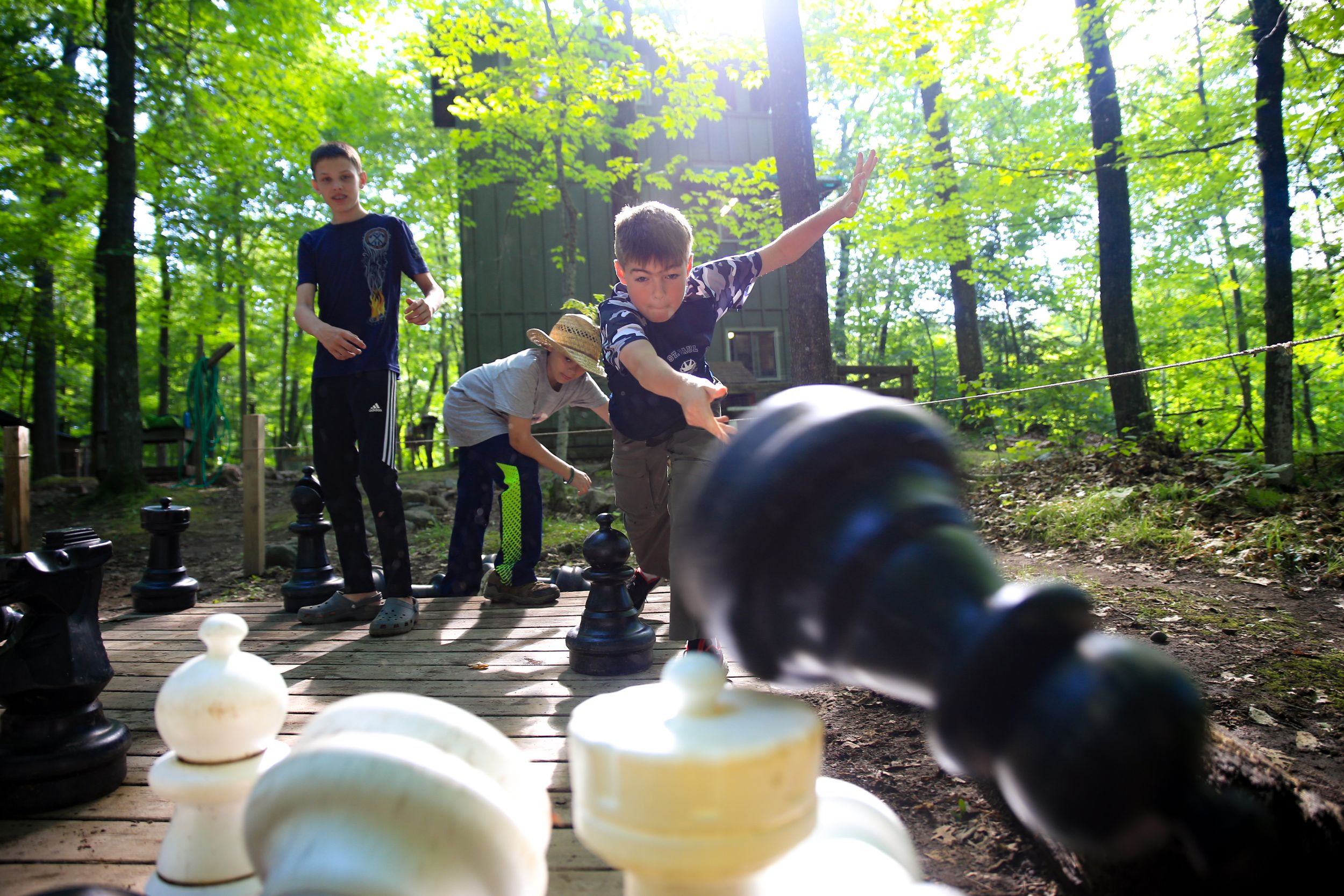 Kids playing with oversized chess pieces in a sunlit forest clearing.