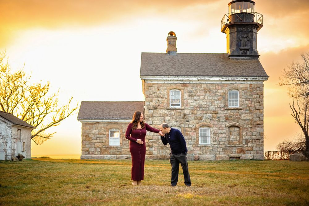 A couple shares a romantic moment at sunset by a lighthouse on a hilltop.
