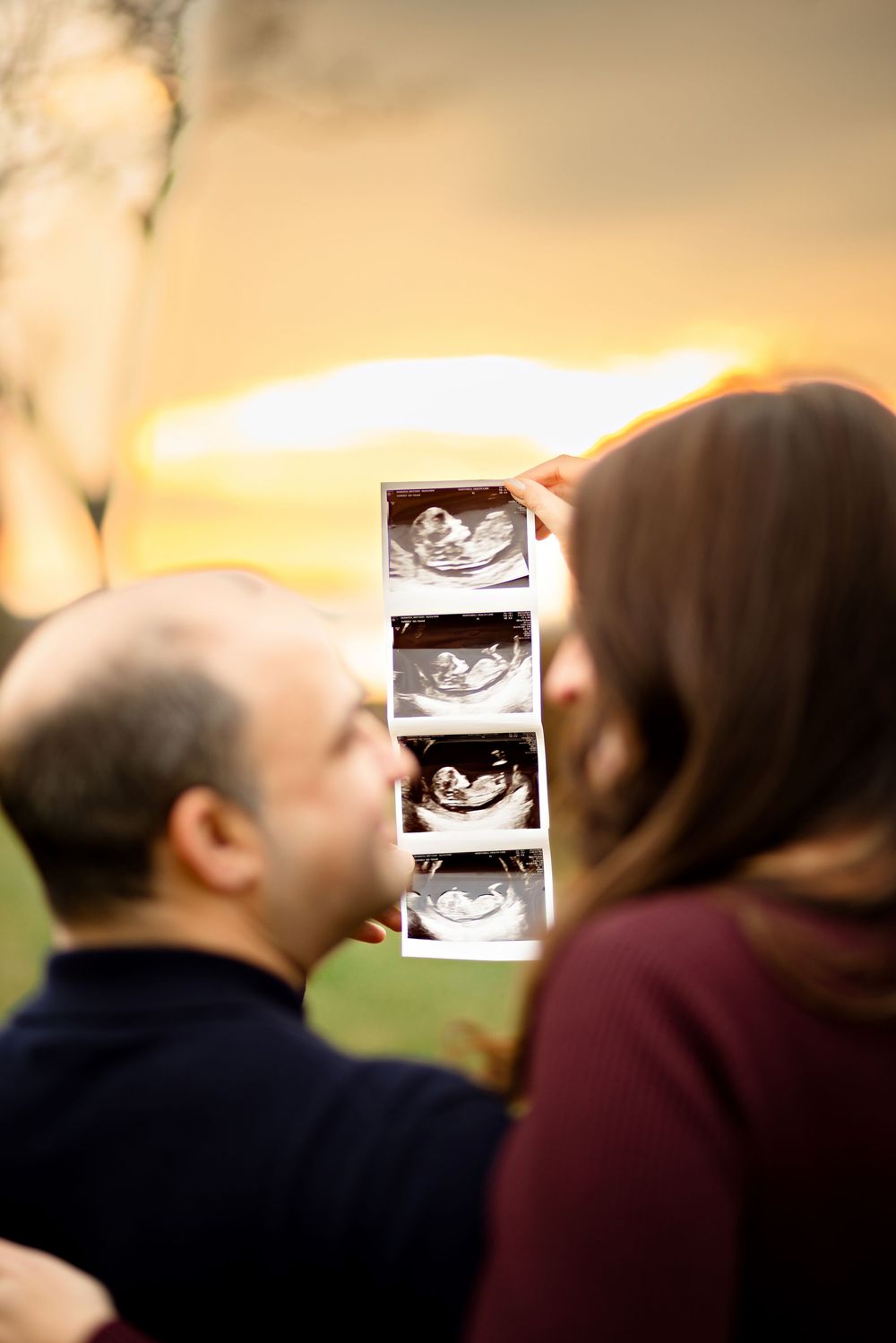 A couple holding up an ultrasound photo during a pregnancy announcement photoshoot at sunset.