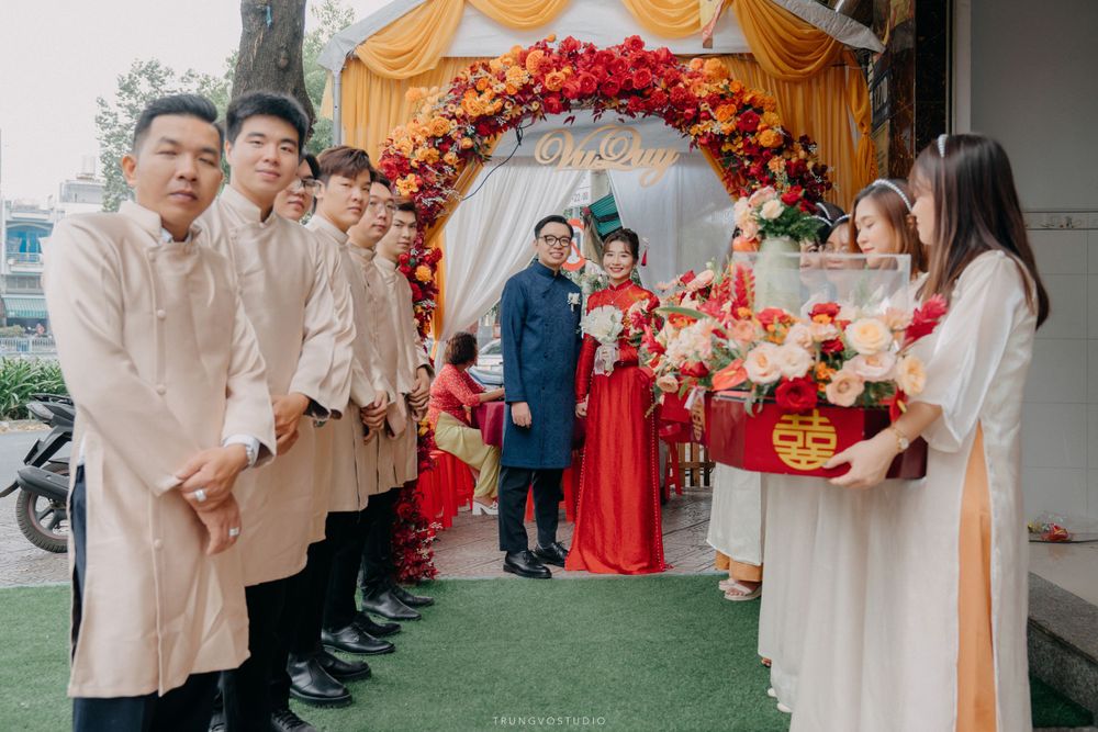 Wedding party in traditional Vietnamese ao dai lines up at floral arch for ceremony procession.