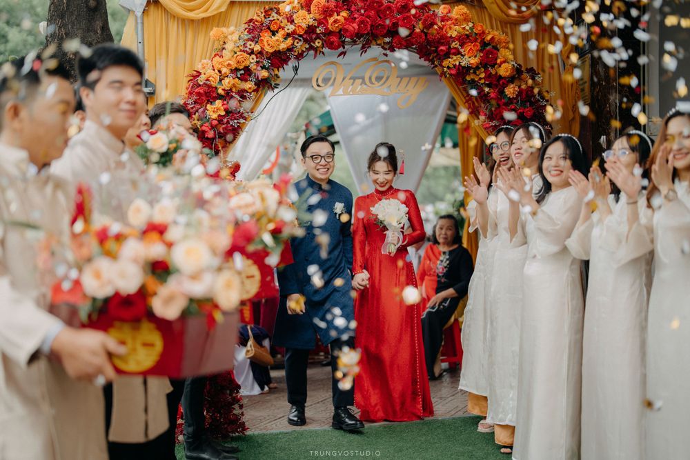 Vietnamese bride and groom walk through flower petal shower at traditional outdoor wedding ceremony.