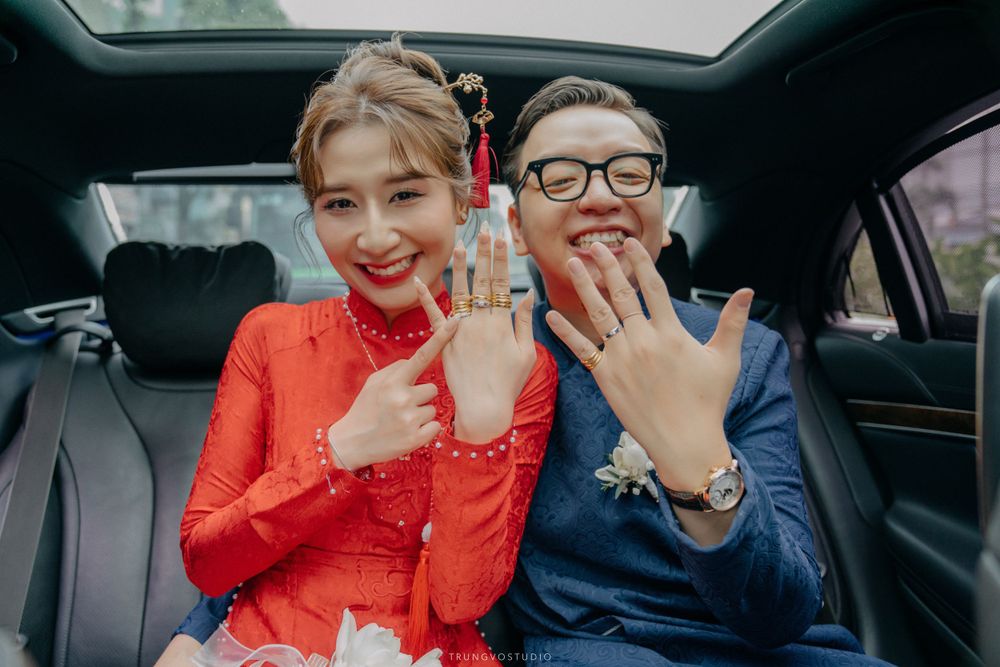 Vietnamese wedding couple in traditional red and blue ao dai show off rings inside a luxury car.