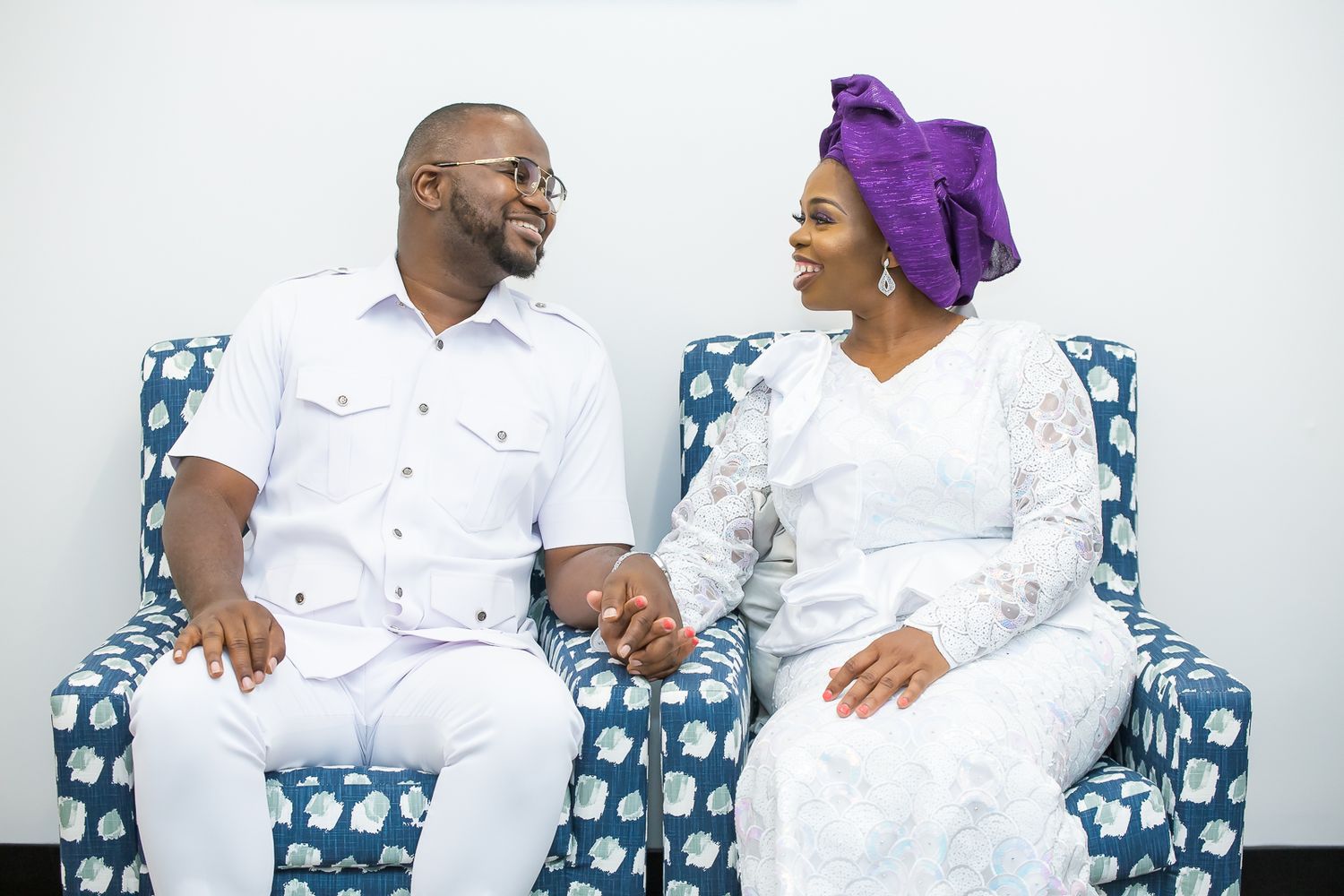 A couple in matching white outfits share a joyful moment while seated on a patterned couch.