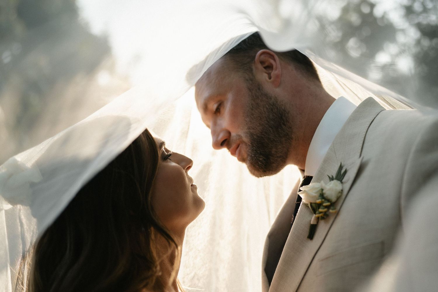 A couple shares an intimate moment at their wedding during golden hour with sunlight creating a dreamy backlit effect.