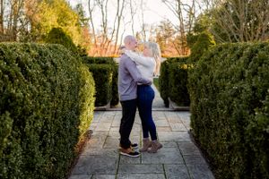 A couple shares a romantic moment on a garden path between tall hedges during golden hour.