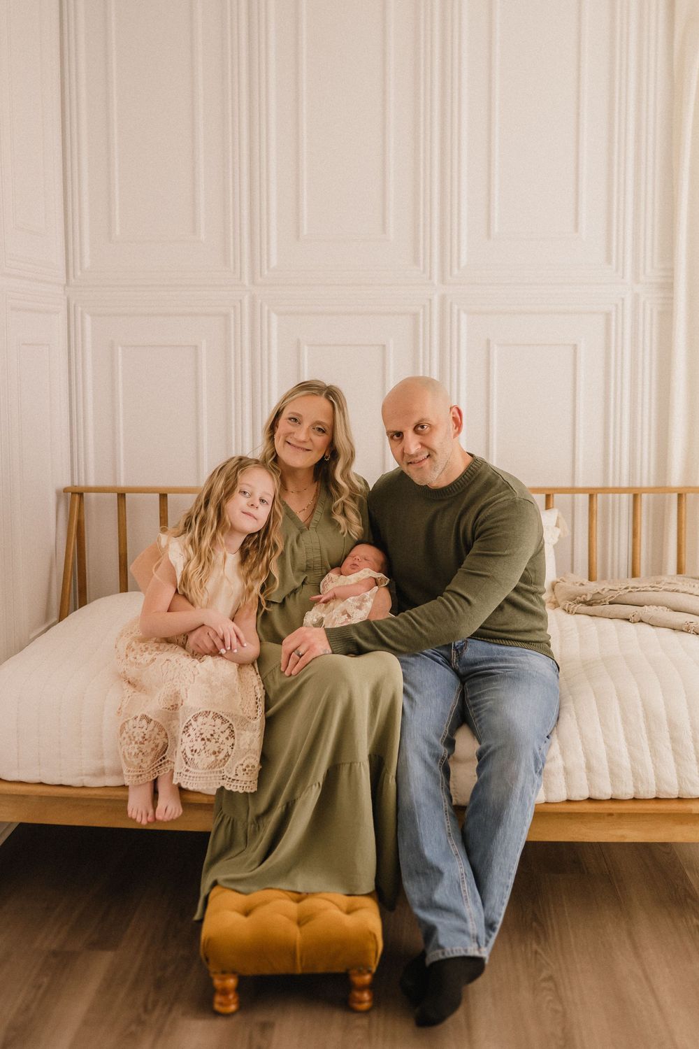 A family portrait in a bedroom with white paneled walls and warm earth tones.