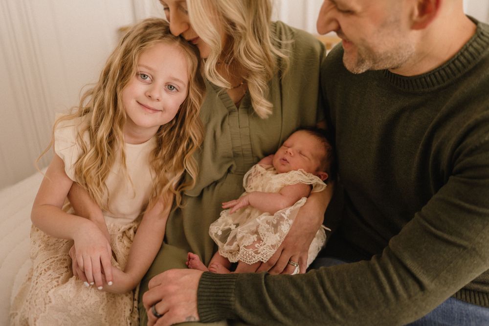 Family sits together on sofa in warm earth tones while holding newborn baby.