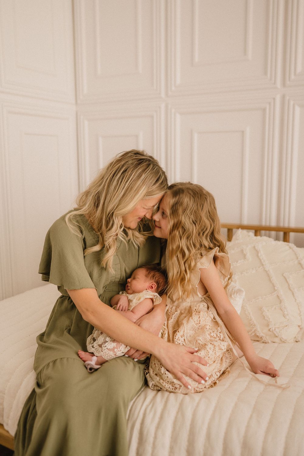 Intimate family moment captured in soft lighting on a bed with sage green and cream tones.