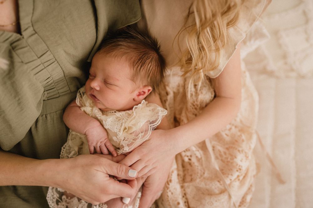 Tender moment of a sleeping newborn in lace clothing being cradled by gentle hands.